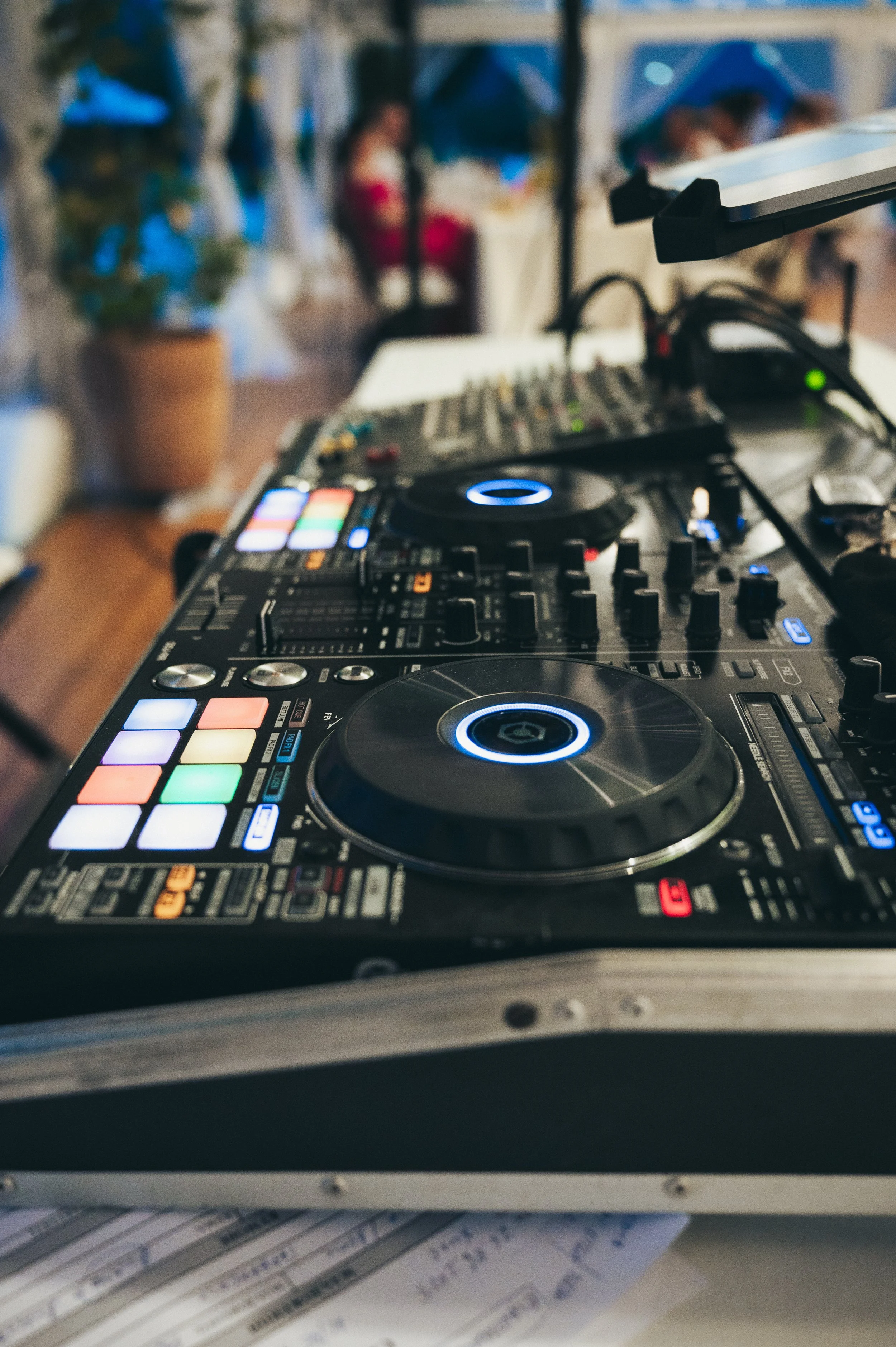 Close-up of DJ mixing console with illuminated buttons and turntables at an indoor event.