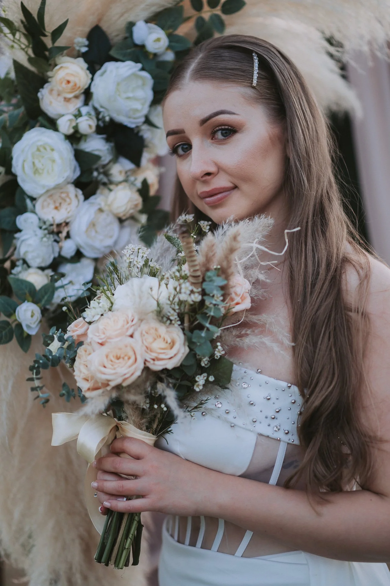 Brunette bride holding a bouquet of roses, eucalyptus, and pampas grass at her wedding.