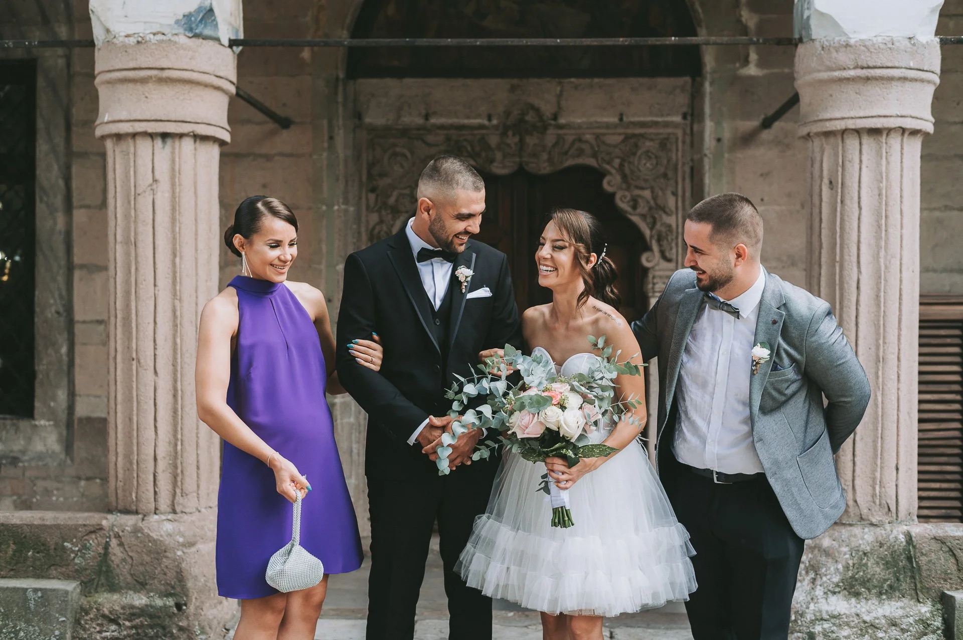 A bride holding a bouquet of flowers standing next to three friends at a wedding, smiling and enjoying the moment.