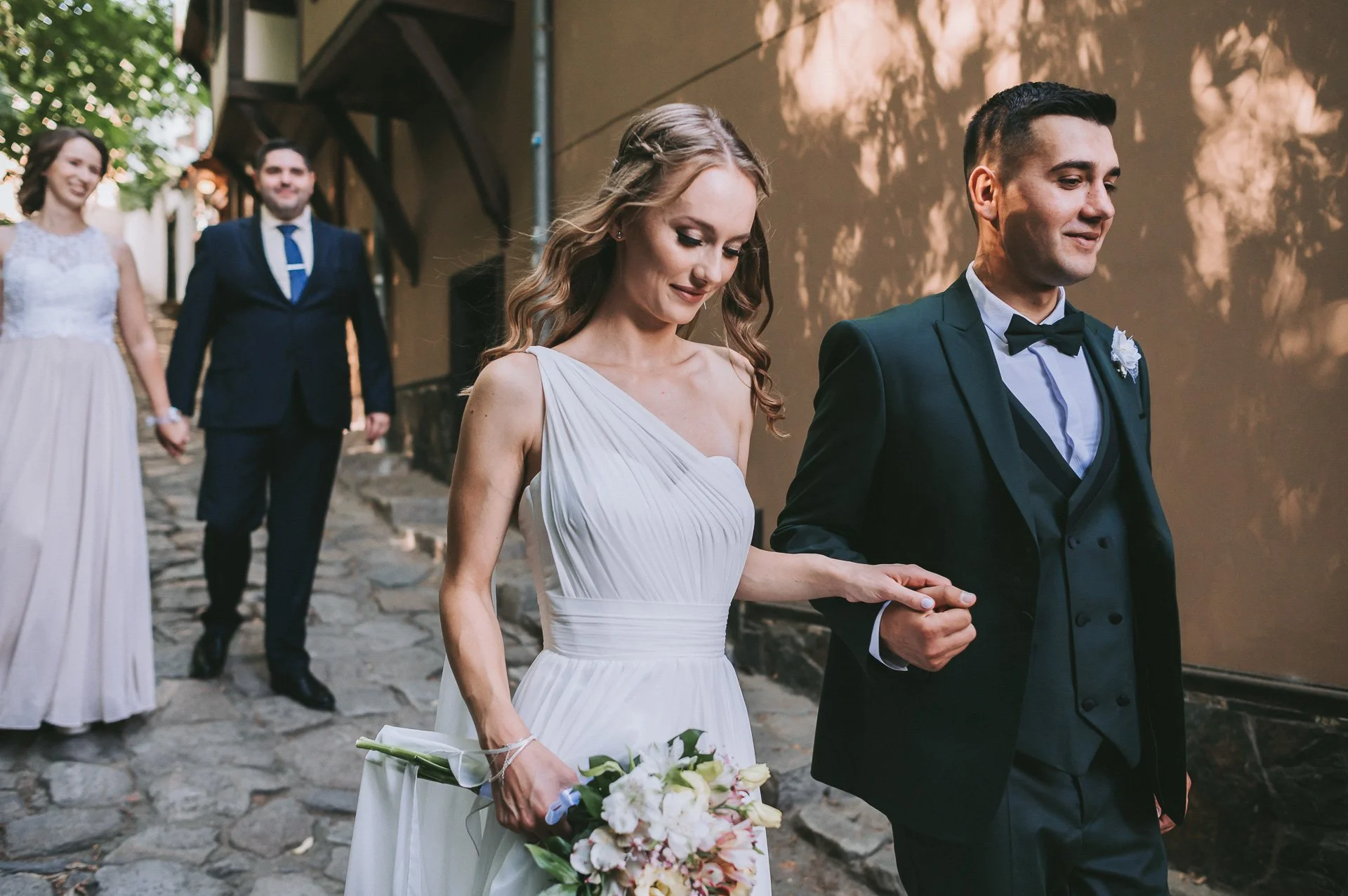 A bride and groom holding hands at their wedding ceremony, with bridesmaids and groomsmen in the background.