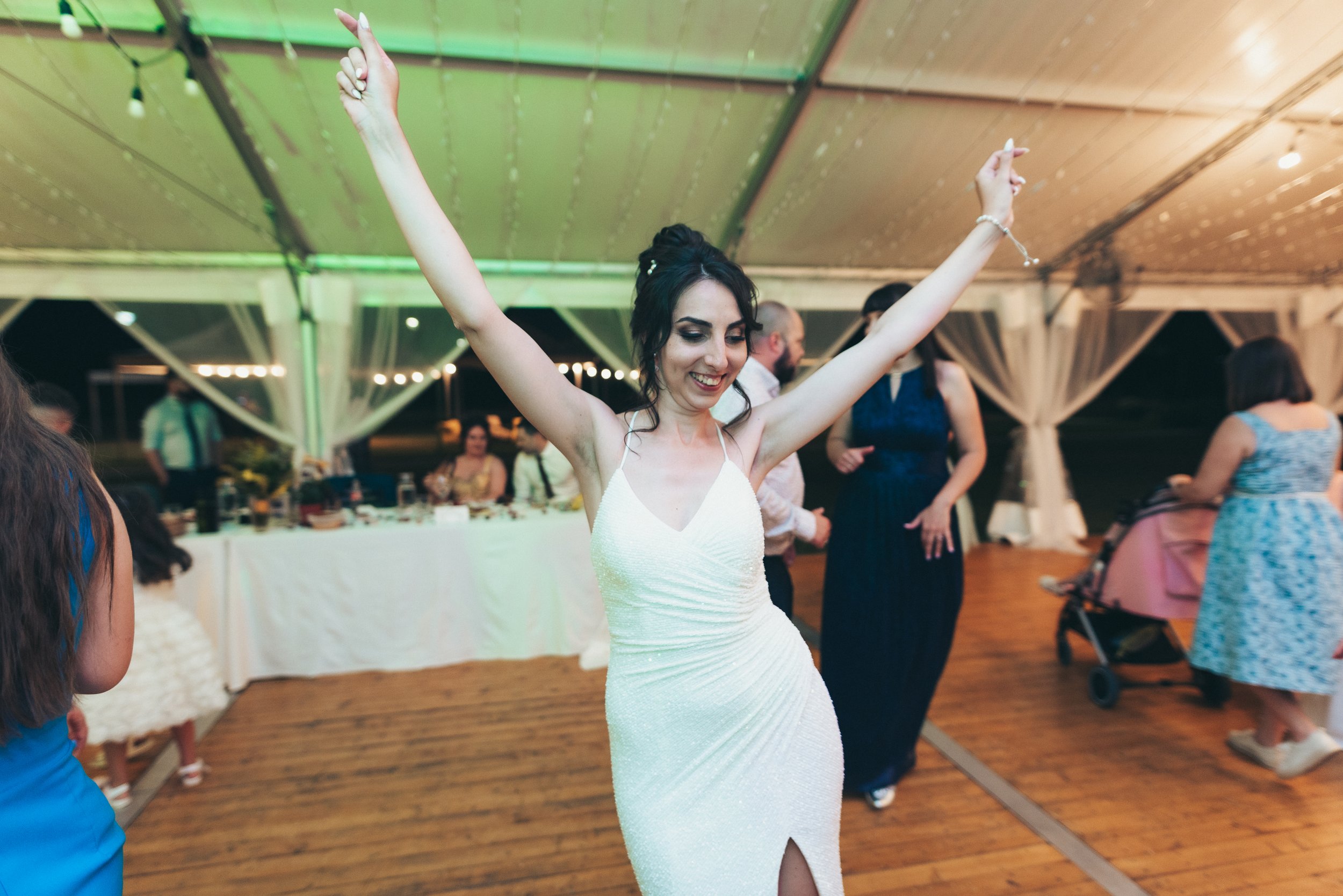 A woman in a white dress dancing with arms raised at an indoor wedding reception.