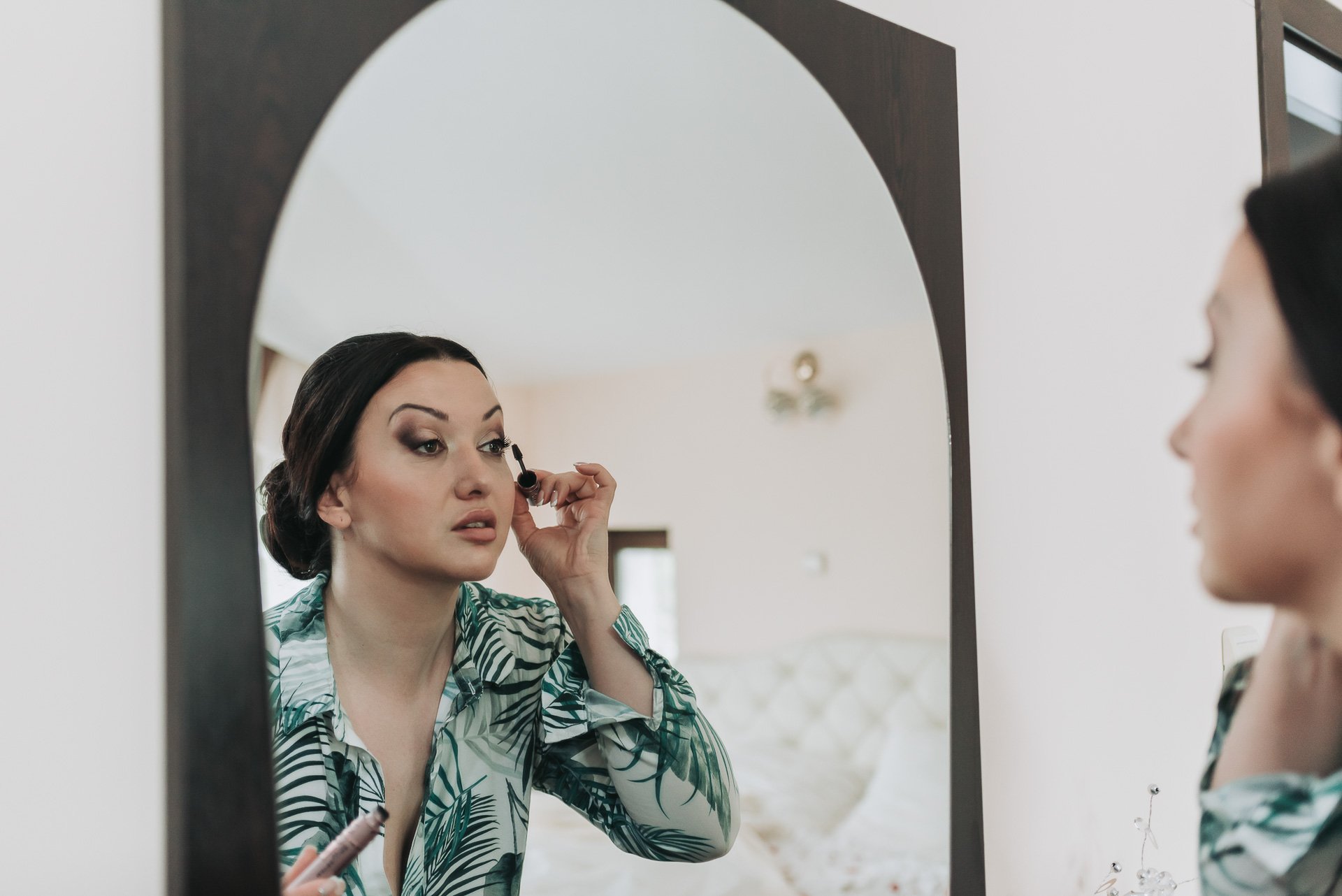 Woman applying makeup while looking at her reflection in a mirror.