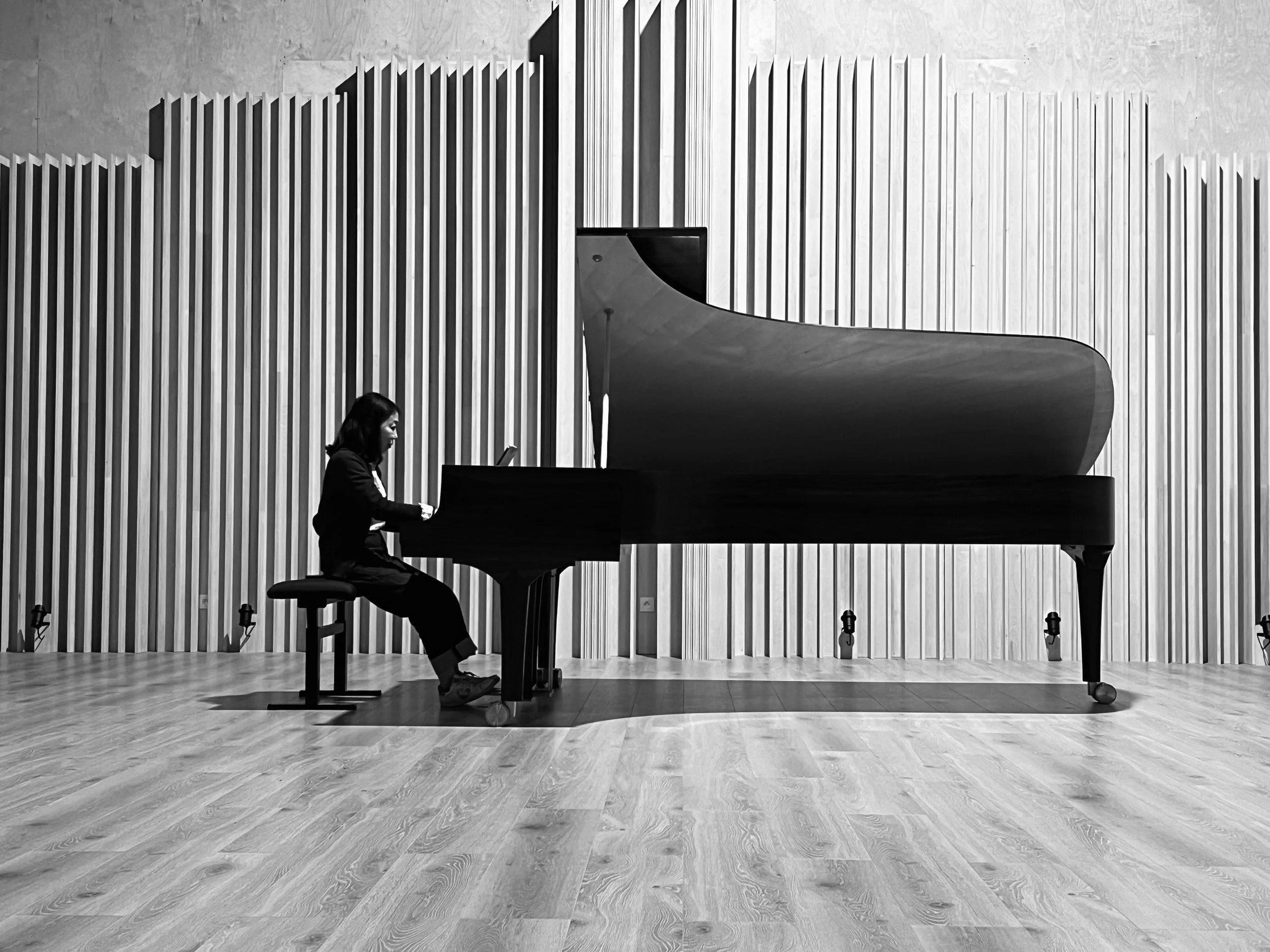 Une femme jouant du piano à queue dans une salle de concert moderne, avec des murs en bois clair et un sol en bois.