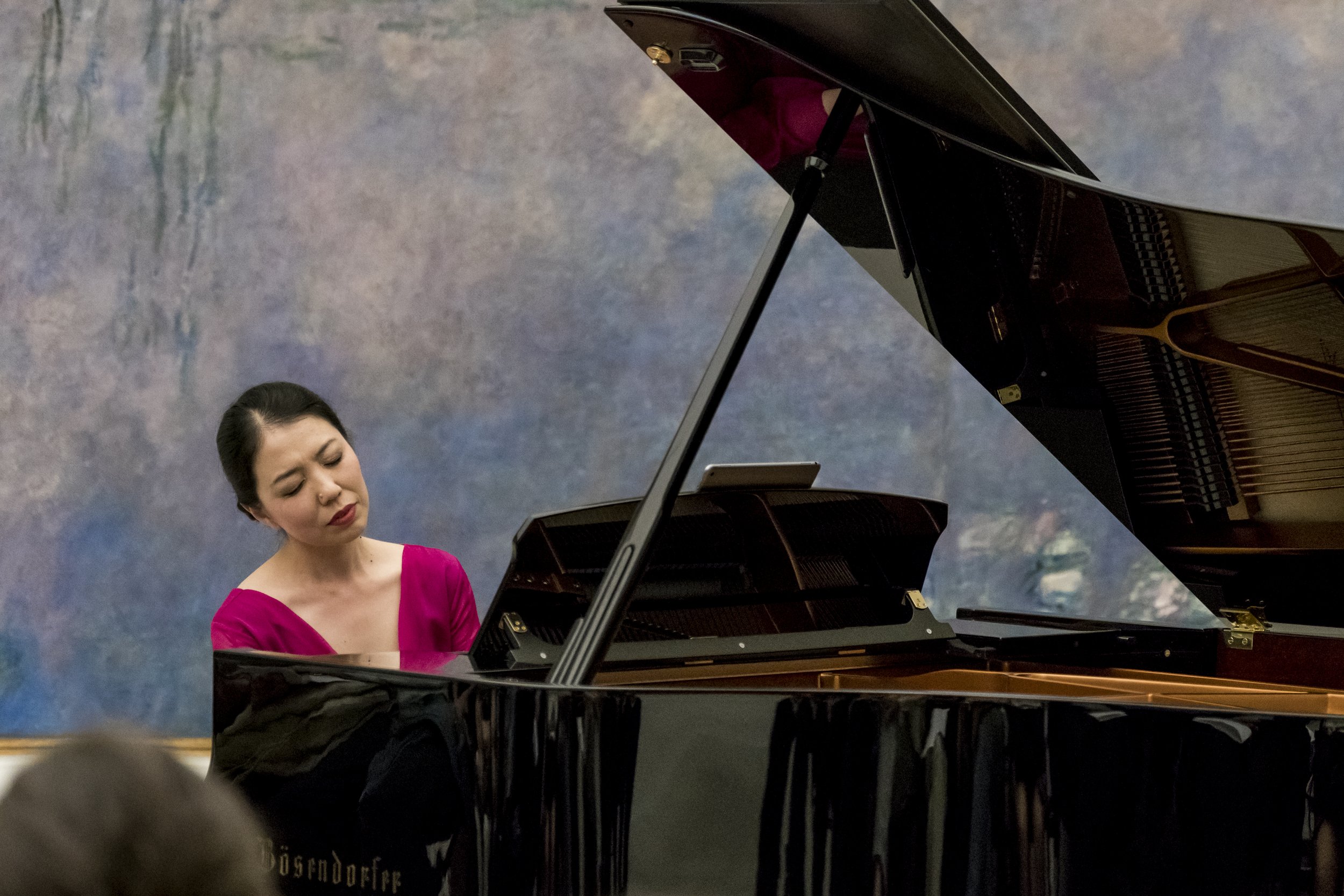Une femme joue du piano à queue dans un cadre intérieur, portant une robe rose.