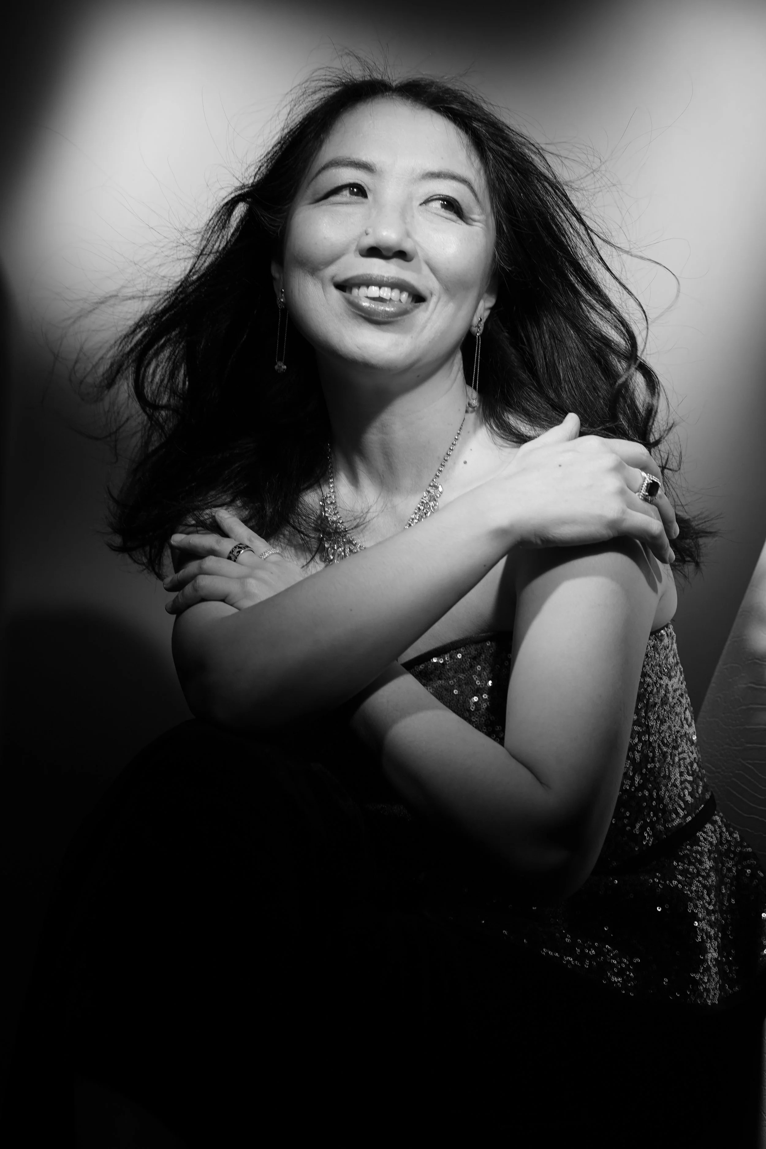 Portrait d'une femme souriante portant des bijoux, en noir et blanc.