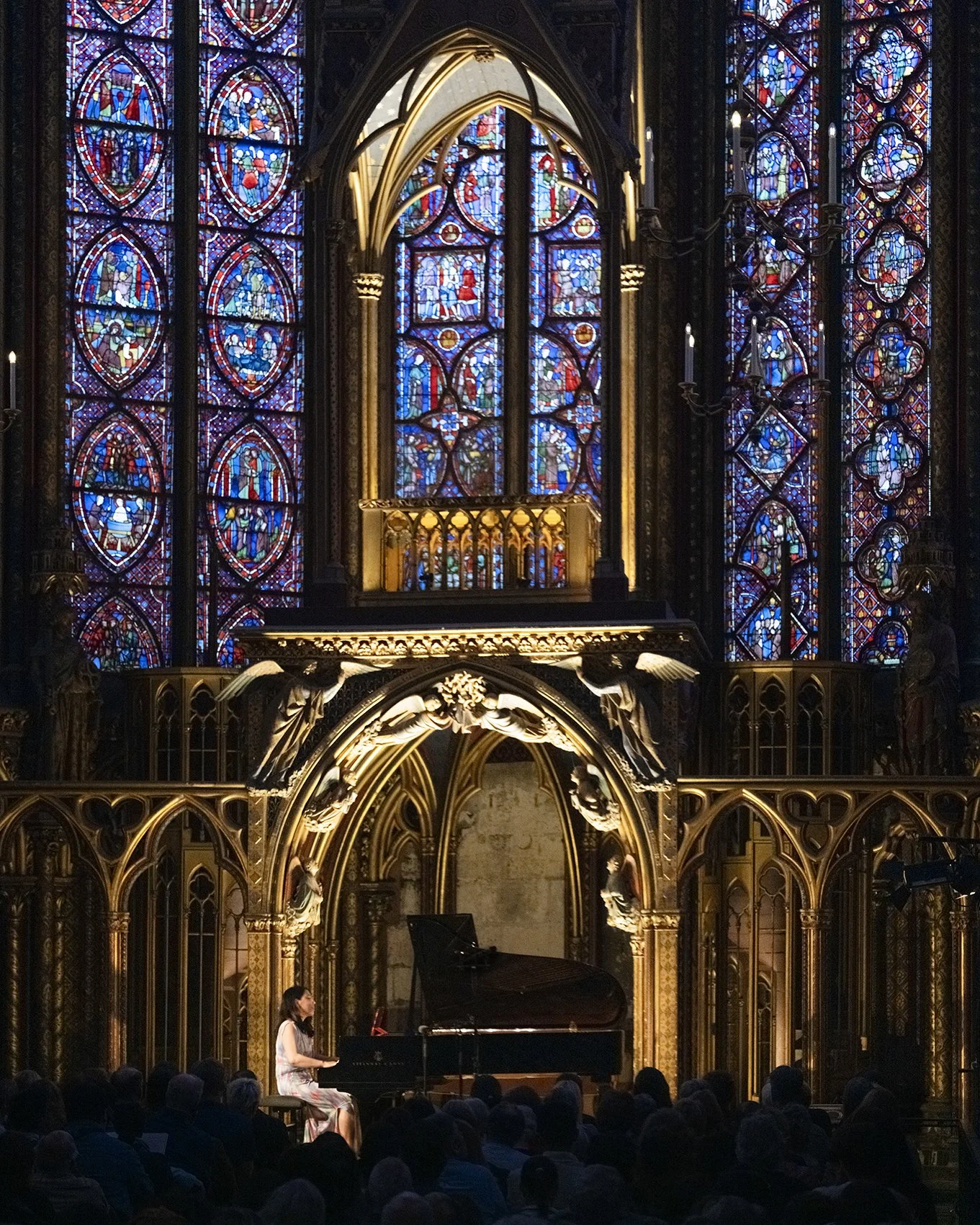 Une performance de piano dans une cathédrale avec de magnifiques vitraux colorés en arrière-plan et un public assis en face.