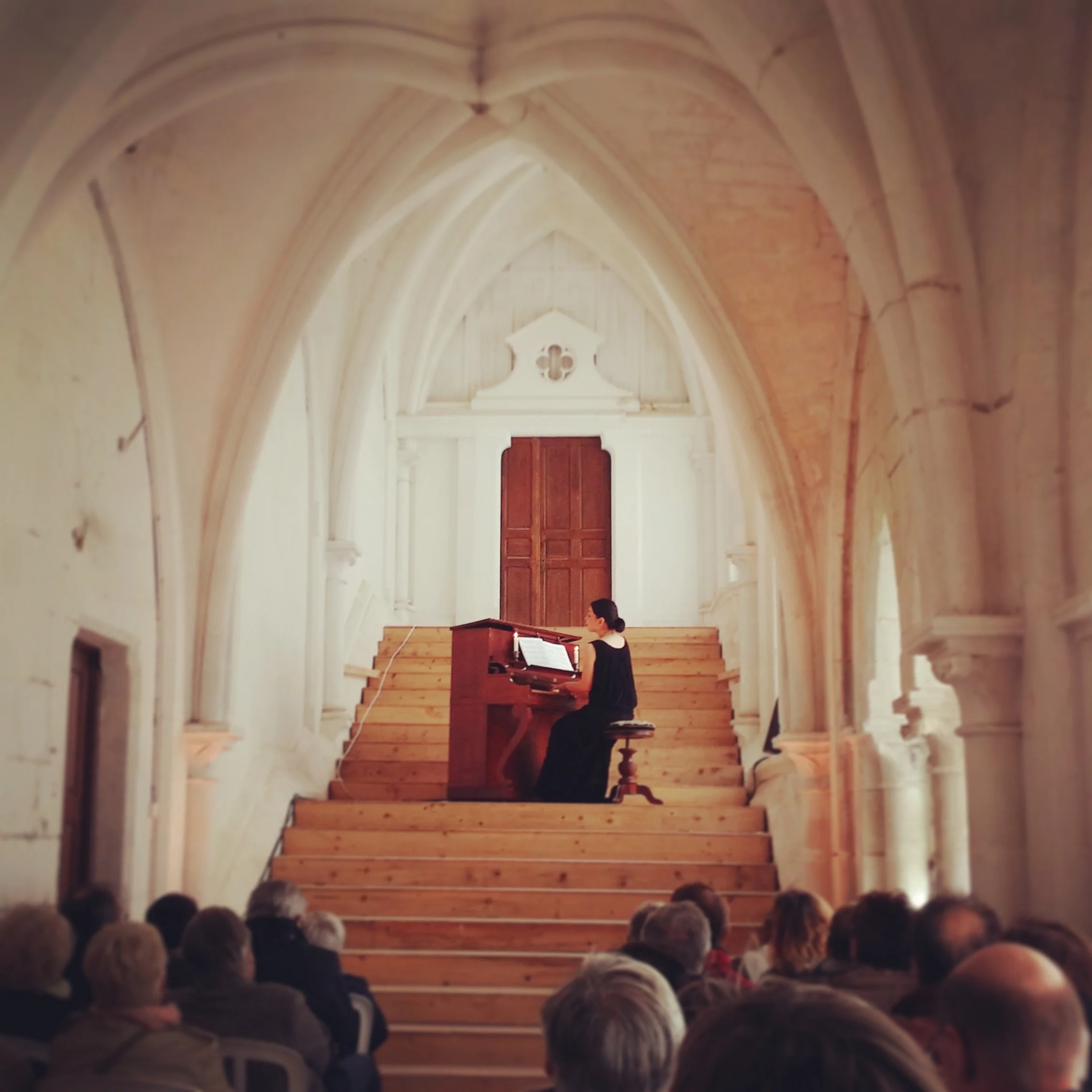 Une femme joue du piano dans une église avec un public assis en face d'elle.