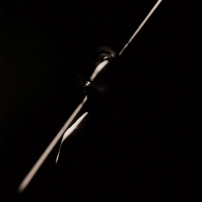 A person in a dark environment with dramatic lighting emphasizing their face and a long line or beam extending from their eye.