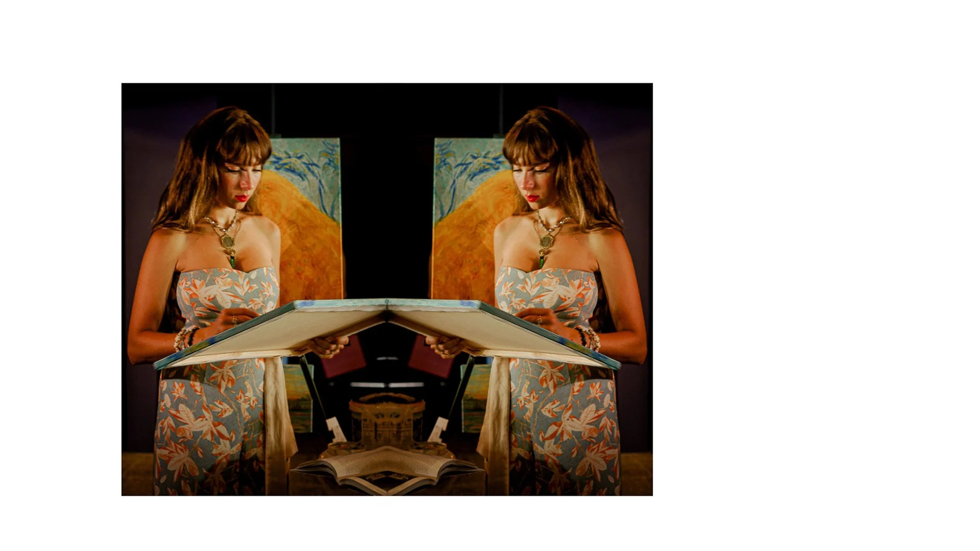 A woman with long brown hair and wearing a floral strapless dress, standing in front of a mirror, looking at an open book.
There are paintings in the background, one of which depicts a mountain landscape with a yellow peak.