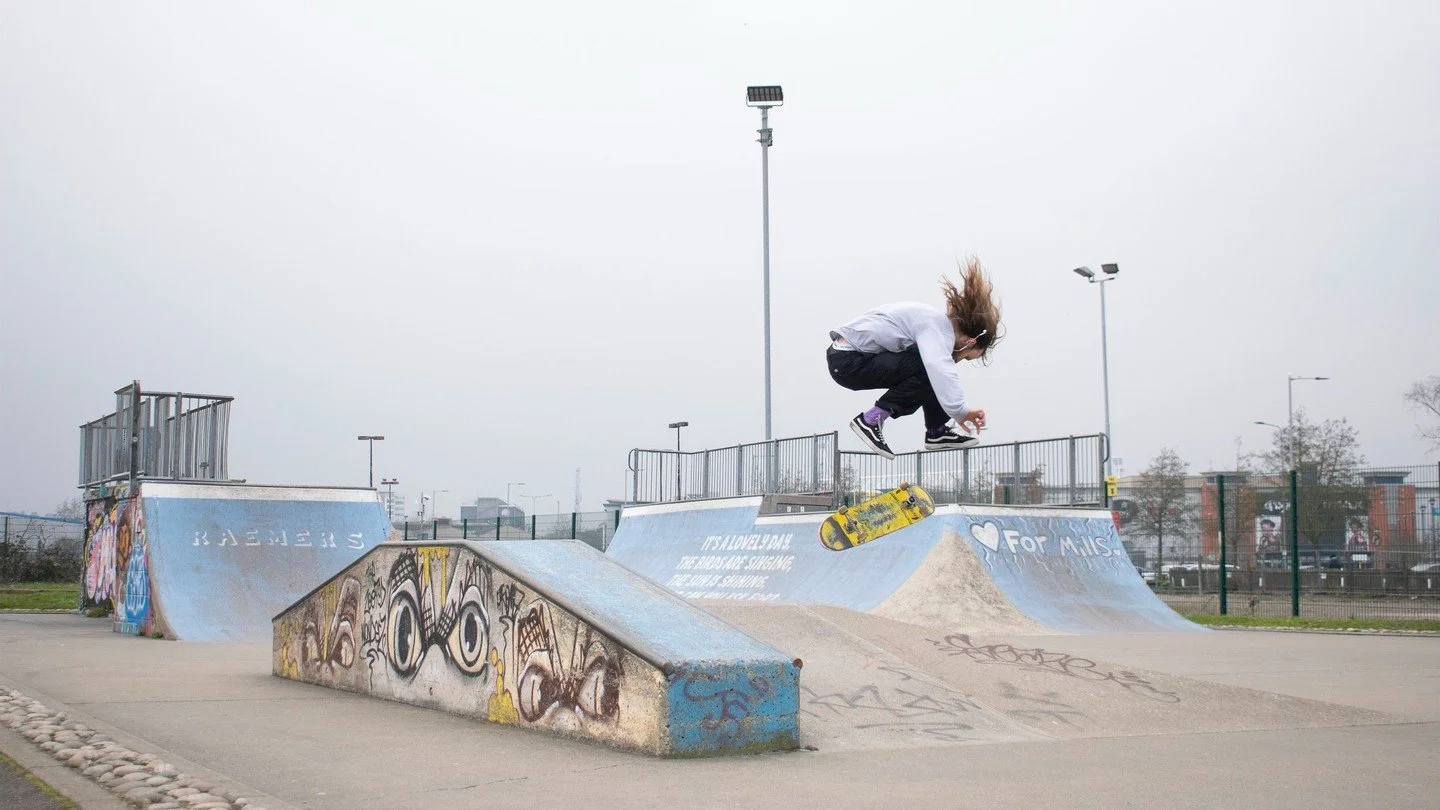 A person skateboarding at a skate park with graffiti on the ramps and overcast sky in the background.