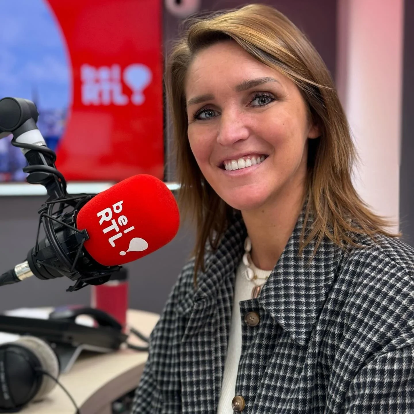Une femme souriante dans un studio de radio devant un micro rouge avec l'inscription « pêl RÎL ».