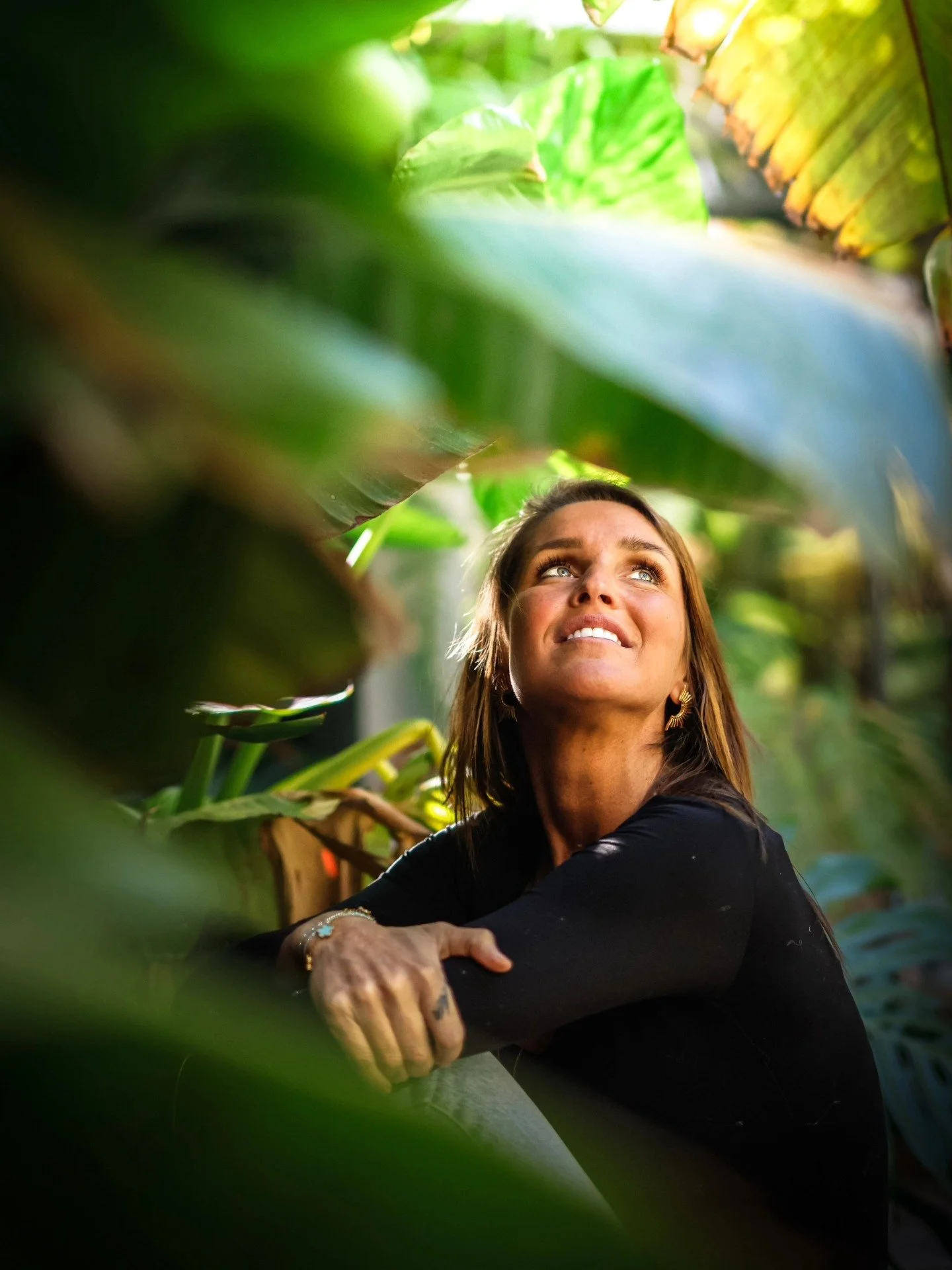 Une femme souriante dans la jungle, entourée de grandes feuilles vertes.