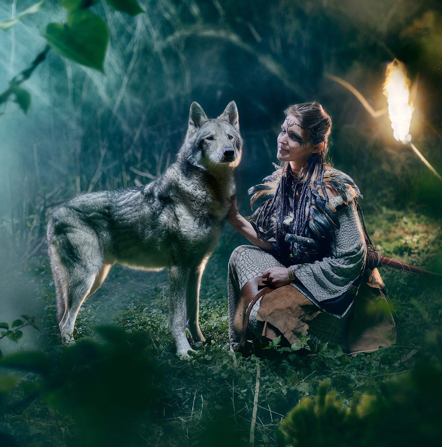Une femme en costume de guerrière avec un maquillage dramatique, assise dans une forêt sombre, caressant un gros chien de type loup.