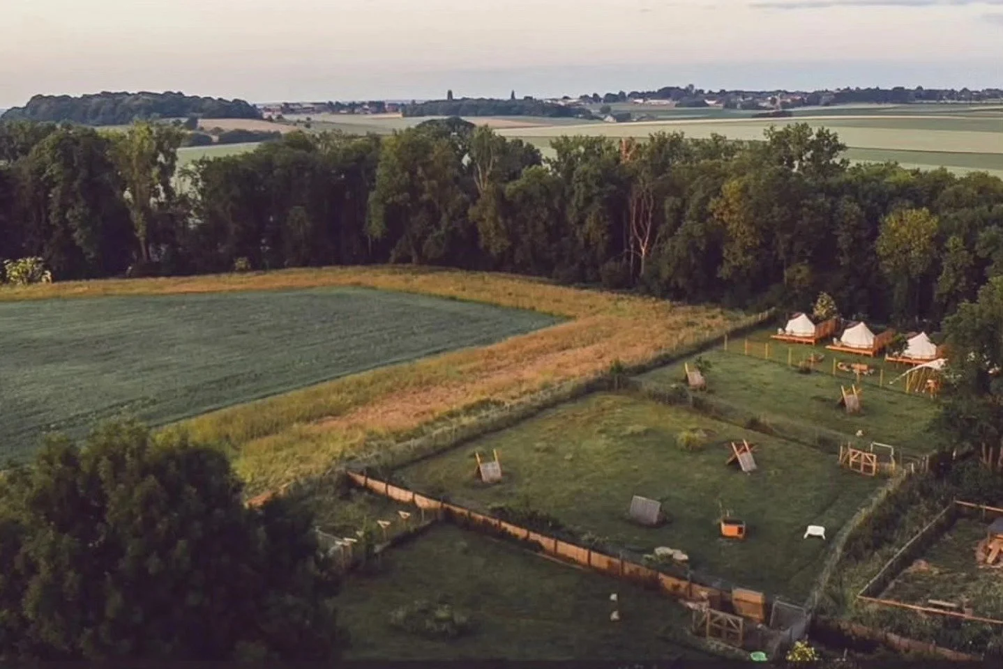 Vue aérienne d'un terrain de jeu ou d'entraînement en plein air, avec des structures pour enfants, entouré d'arbres, avec des champs agricoles au loin.