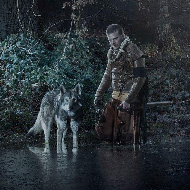 Une personne en tenue médiévale avec un loup dans une forêt humide.