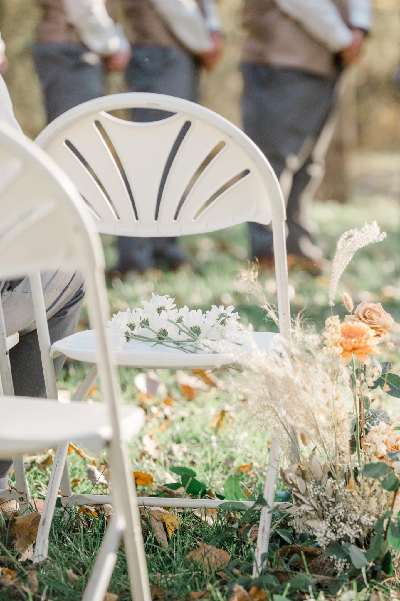 Outdoor event setup with white chairs, floral arrangements, and fall foliage.