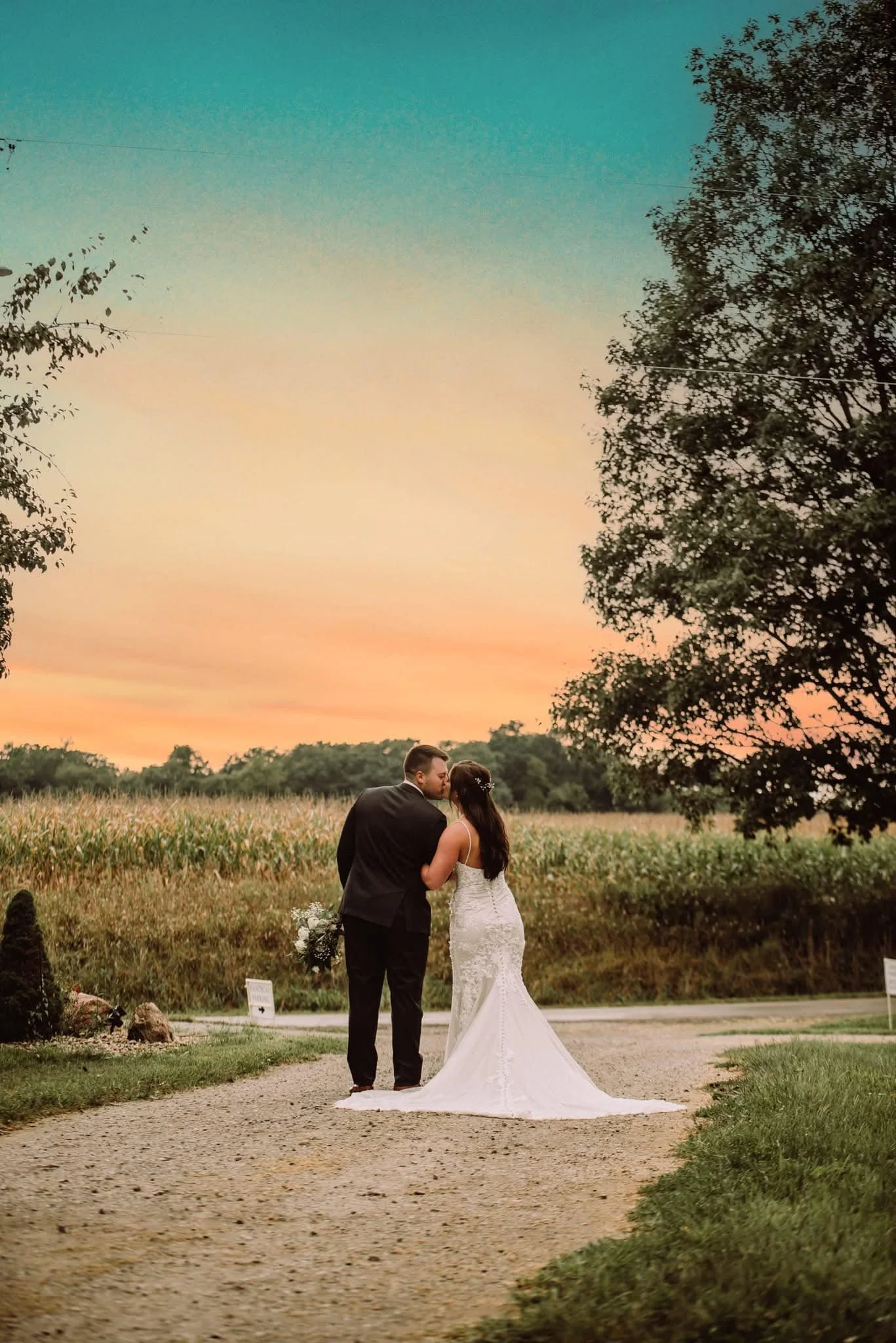 An outdoor wedding scene at sunset with a bride and groom in a natural setting with trees and open field in the background.