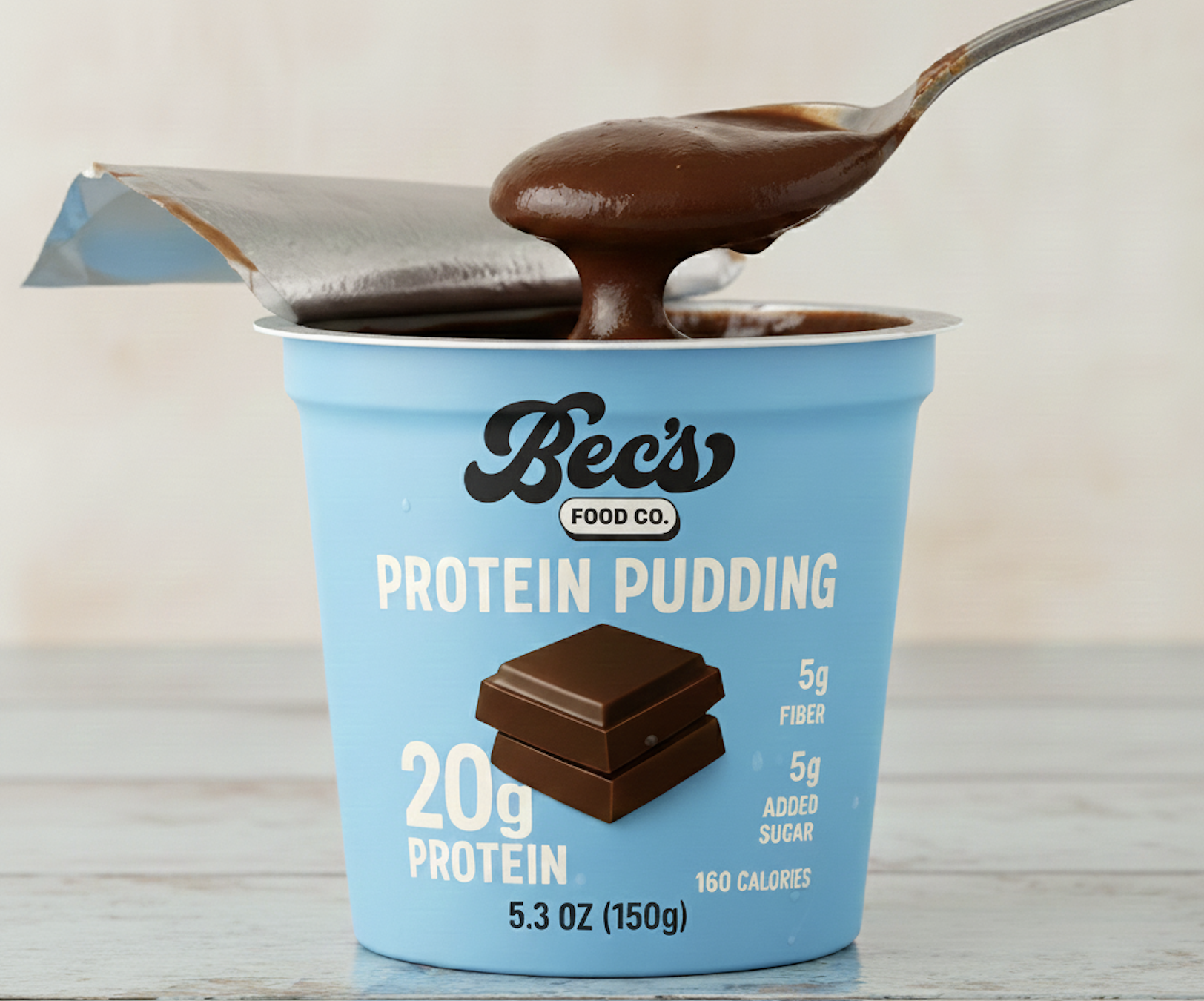 A blue cup of Bec's Protein Pudding with a spoonful of chocolate pudding above the cup.