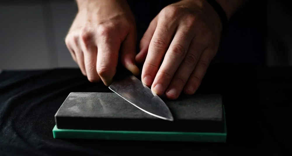 Close-up of hands sharpening a knife on a whetstone.