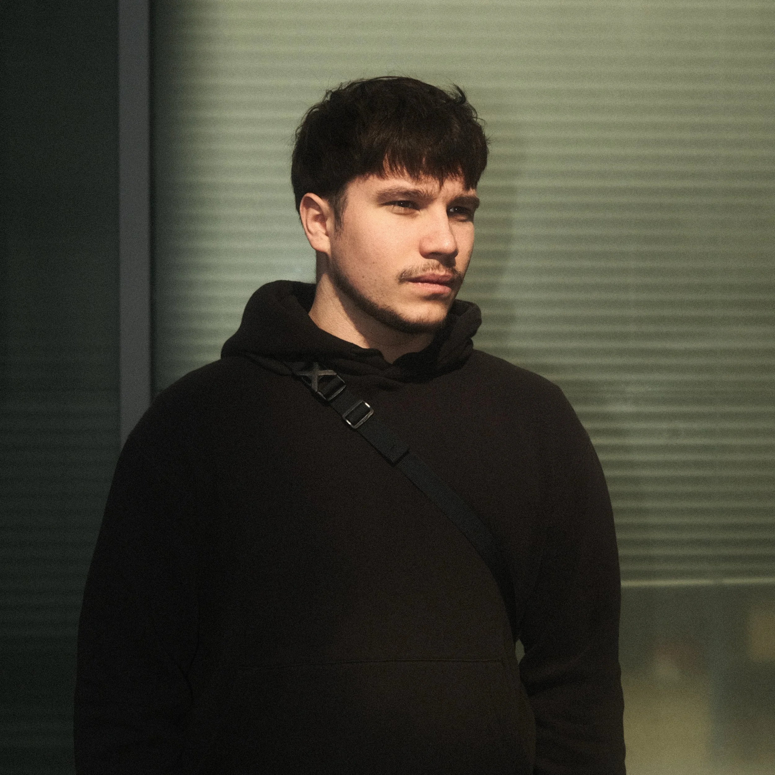 Un jeune homme portant un sweat à capuche noir, regardant pensivement, dans un environnement intérieur