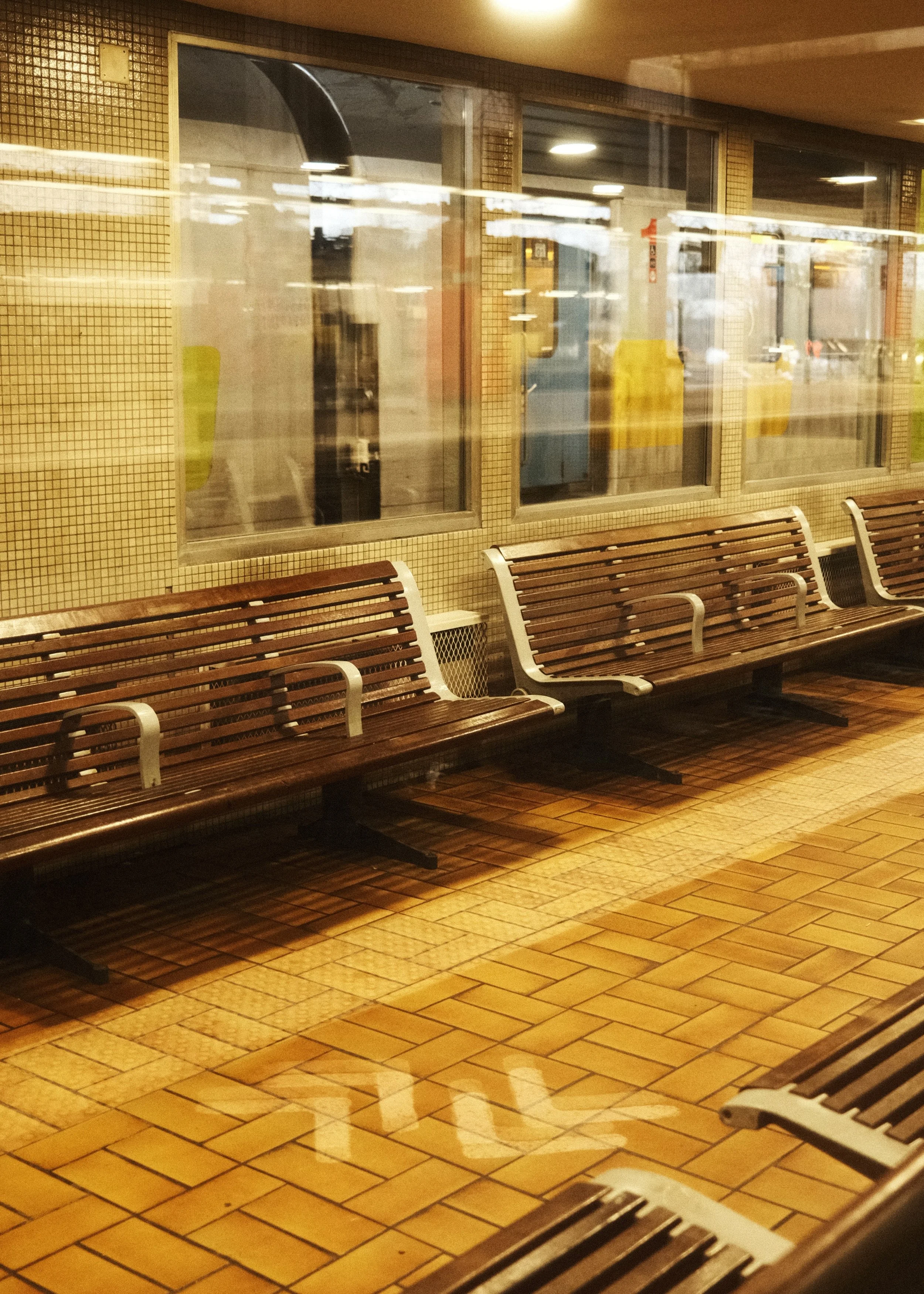 Verrière donnant sur une salle d'attente avec des bancs en bois, dans une gare, avec des fenêtres et un sol en carreaux de terre cuite.