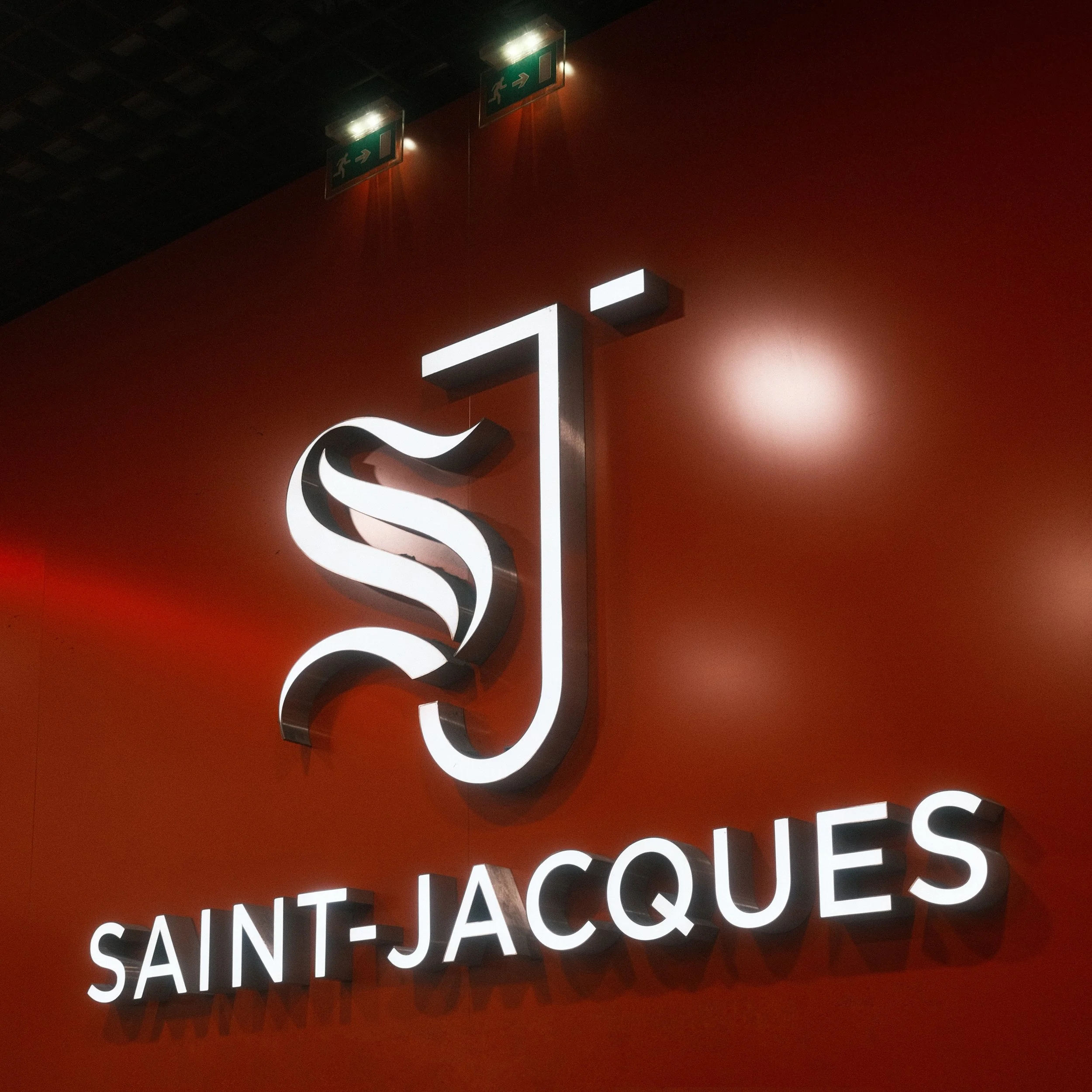 Logo lumineux avec le nom 'SAINT-JACQUES' sur un mur rouge.