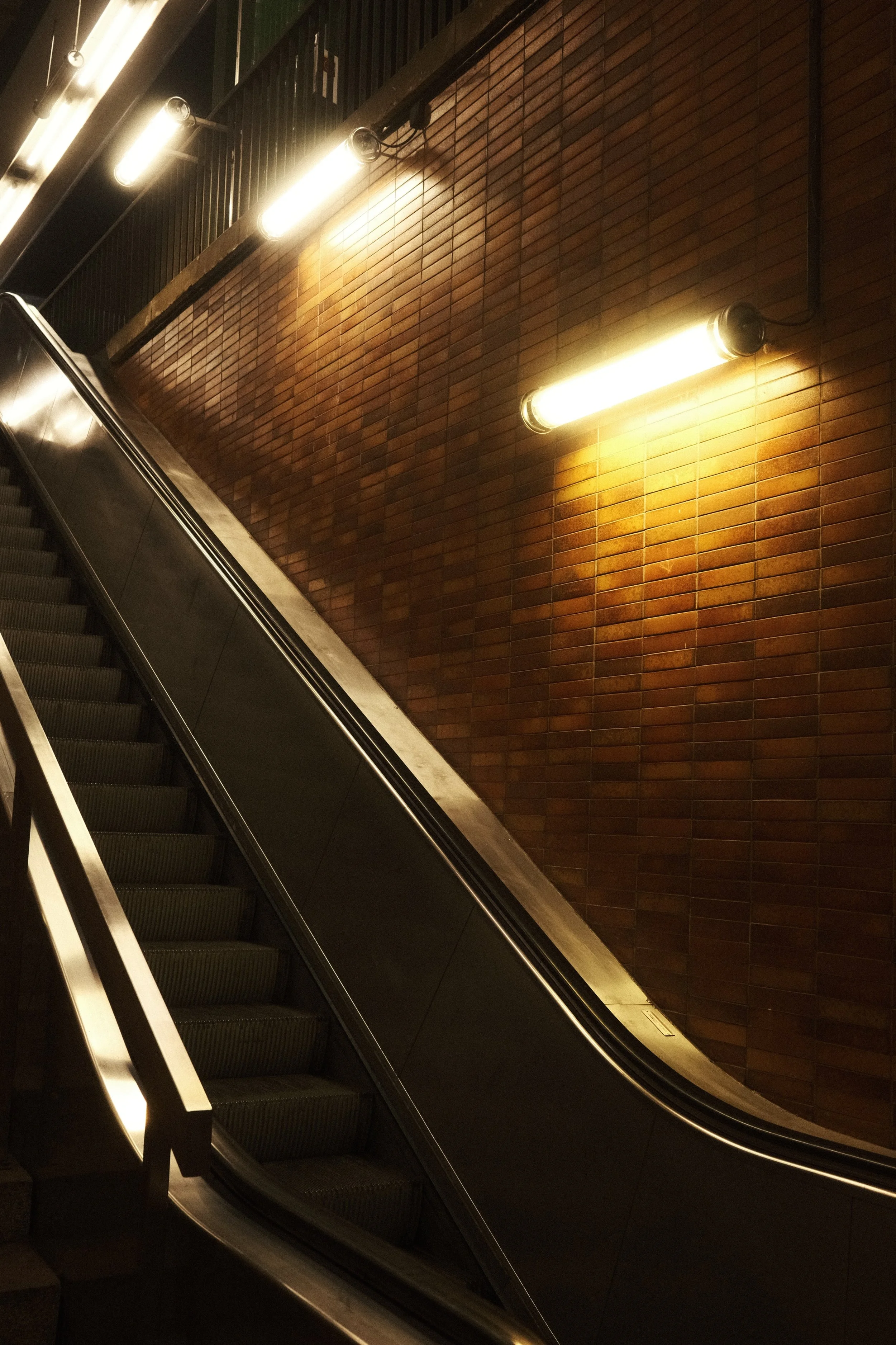 Escalier mécanique dans un espace intérieur avec mur en briques et éclairage au plafond.
