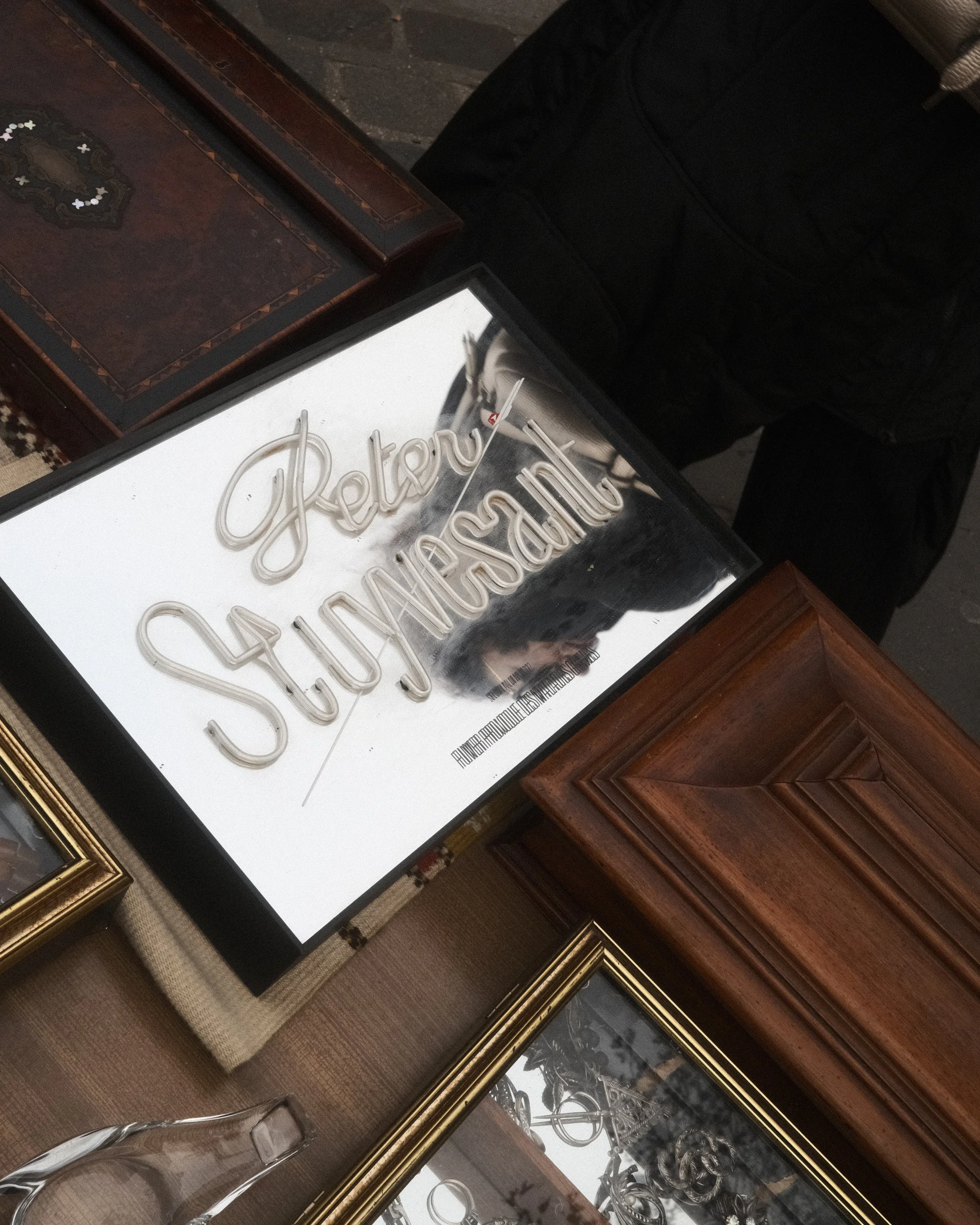Un miroir avec l'inscription 'Retro Suède' en lettres lumineuses, posée sur une table en bois avec plusieurs cadres et objets décoratifs autour.