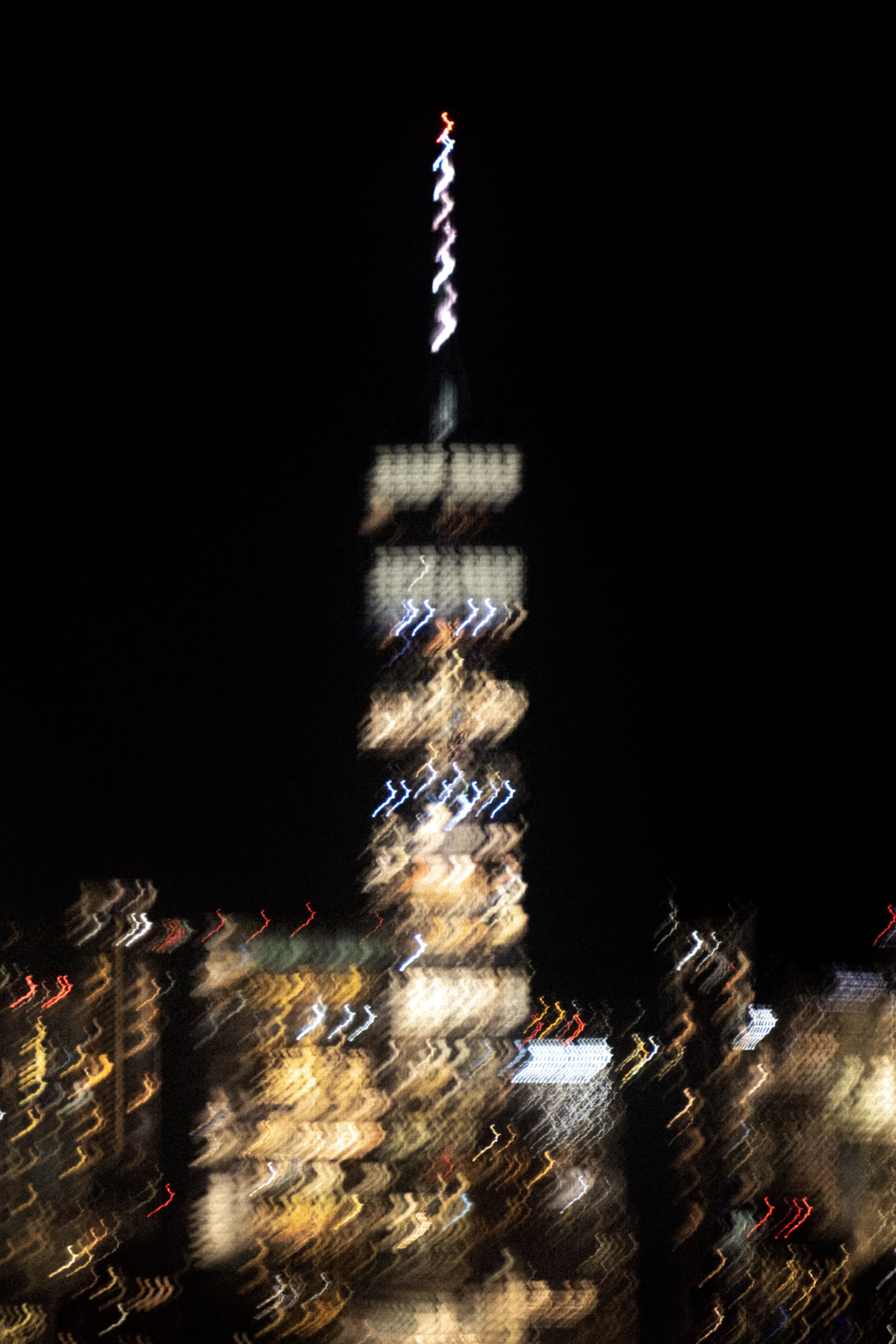 Photo floue d'une tour éclairée la nuit à New York, avec des lumières colorées scintillantes et un ciel noir d'arrière-plan.
