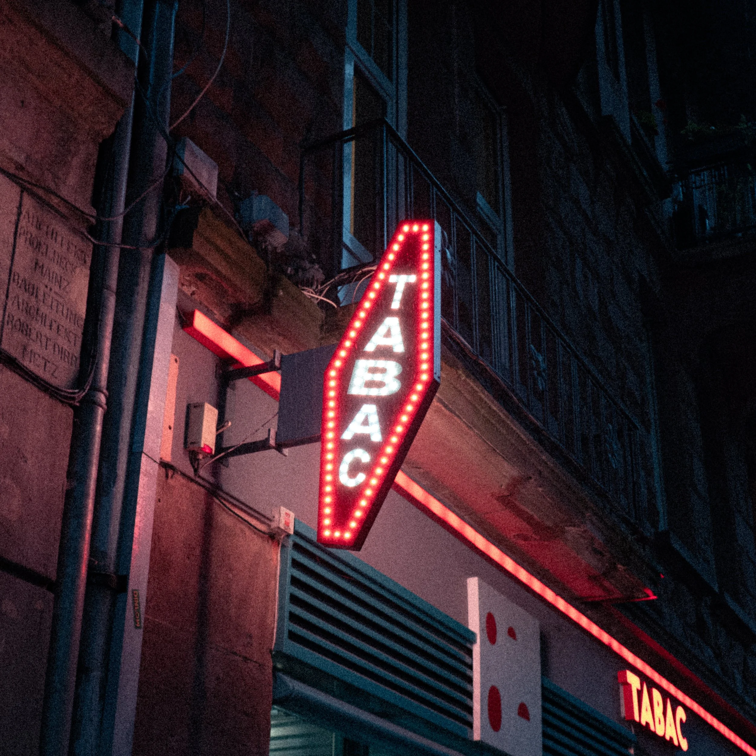 Panneau de signalisation lumineux indiquant un tabac, en soirée ou la nuit, dans une rue urbaine.