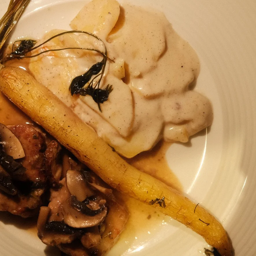 Plat de nourriture contenant des pommes de terre, une carotte, des champignons et une sauce blanche avec des herbes.