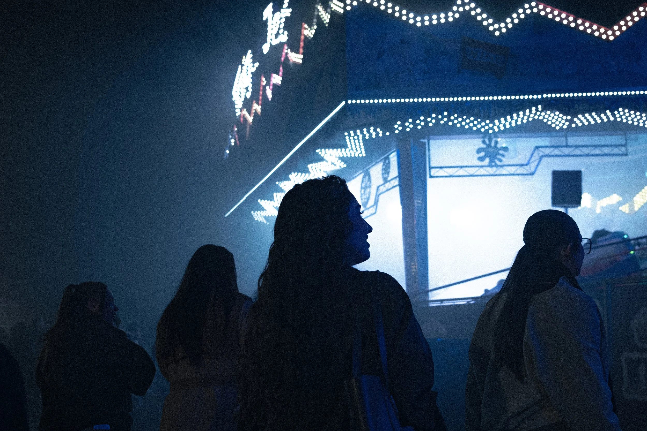 Des personnes regardant une attraction nocturne avec des lumières décoratives dans une fête foraine, ambiance sombre avec des lumières vives