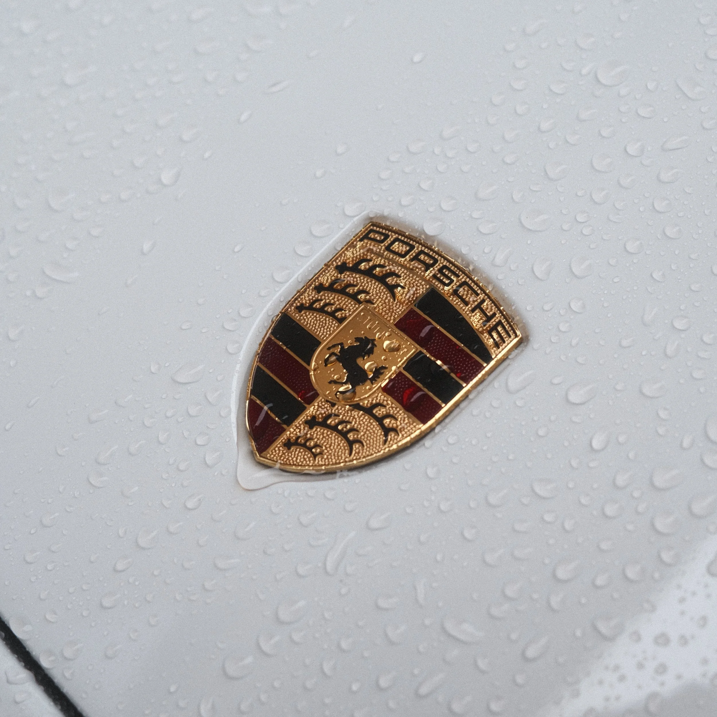Logo de Porsche sur une surface blanche mouillée avec des gouttes d'eau.