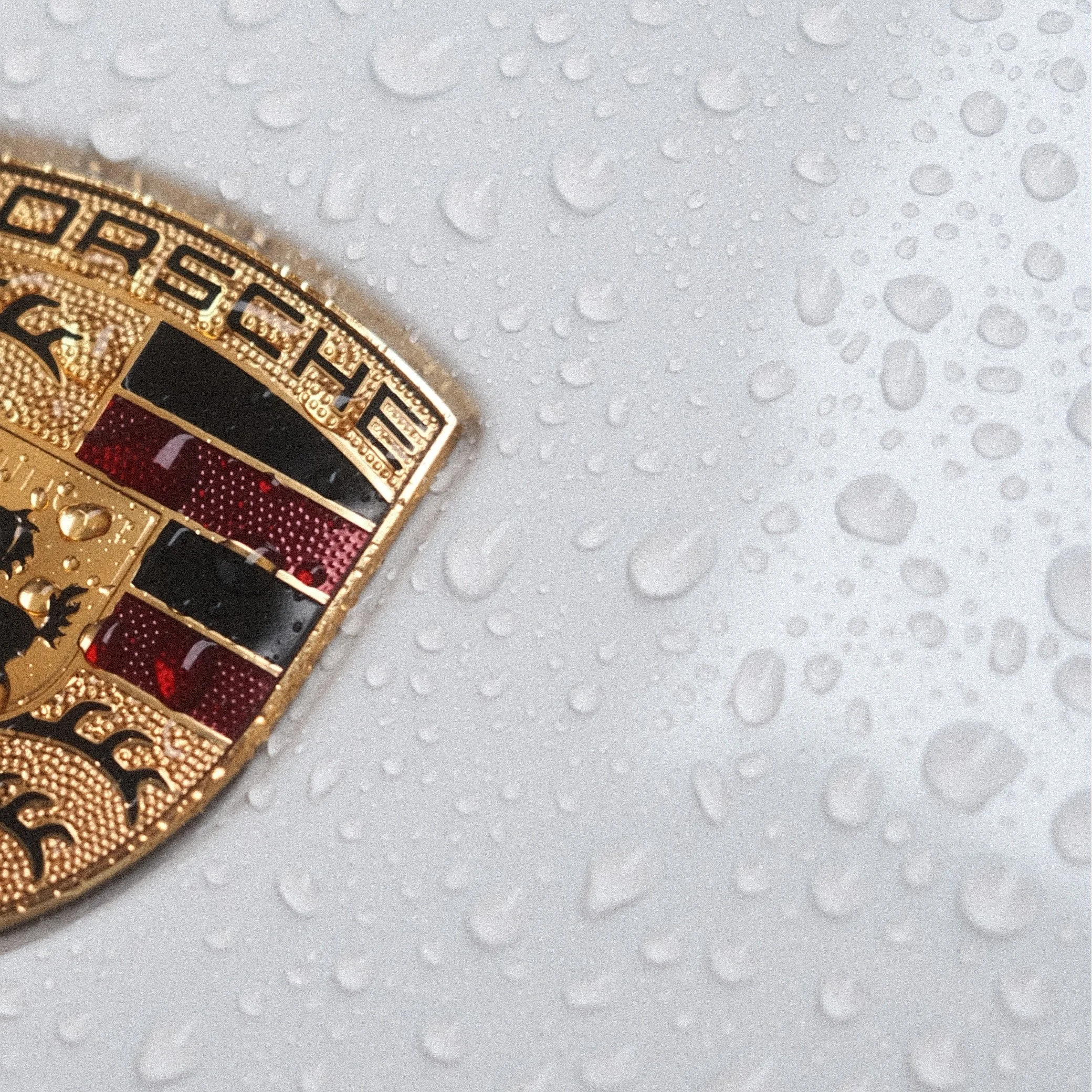 Une badge rond en or avec des détails en noir et rouge, posé sur une surface blanche mouillée avec des gouttelettes d'eau.