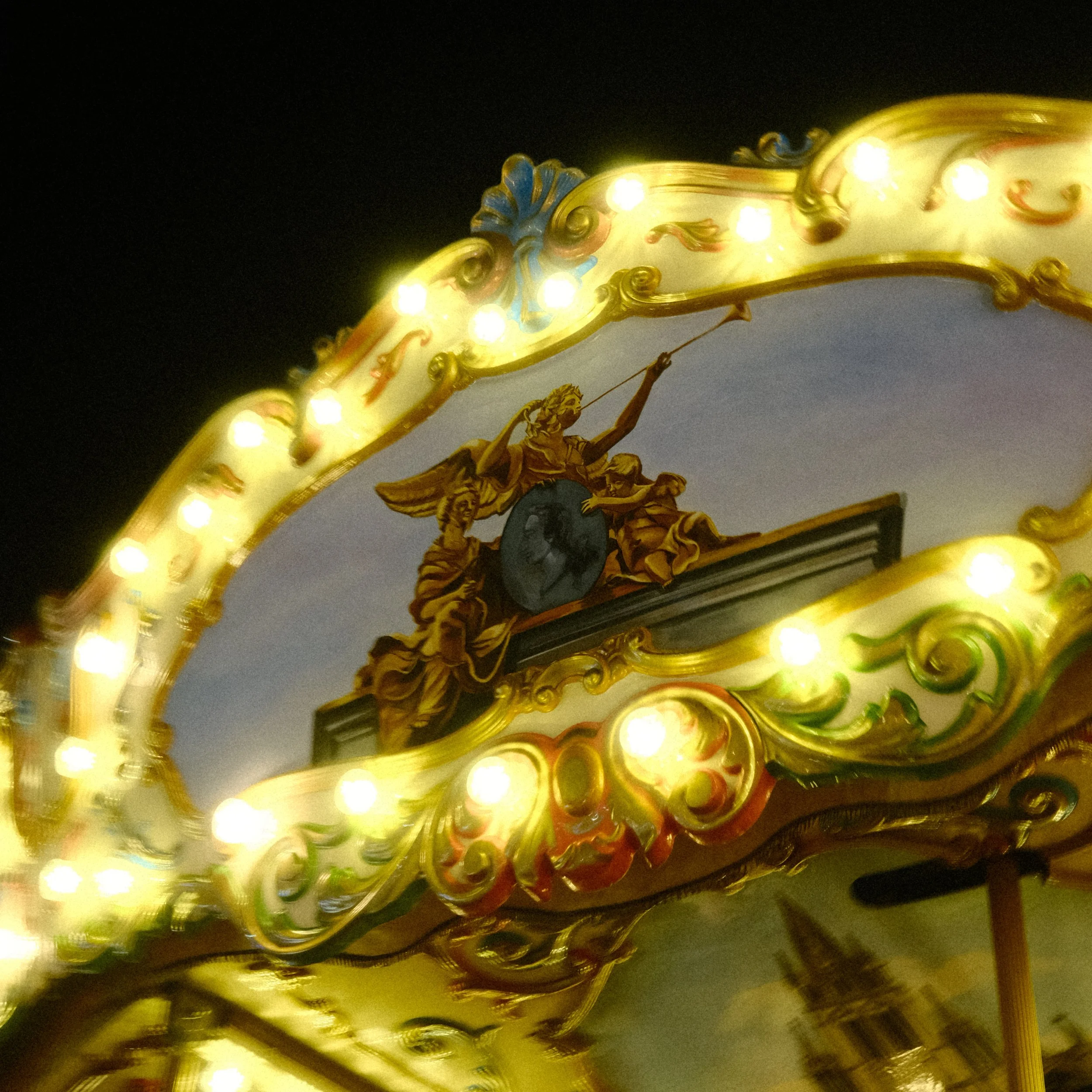 Tourniquet de manège avec lampes lumineuses et sculpture dorée représentant une figure ailée tenant une épée et un bouclier.