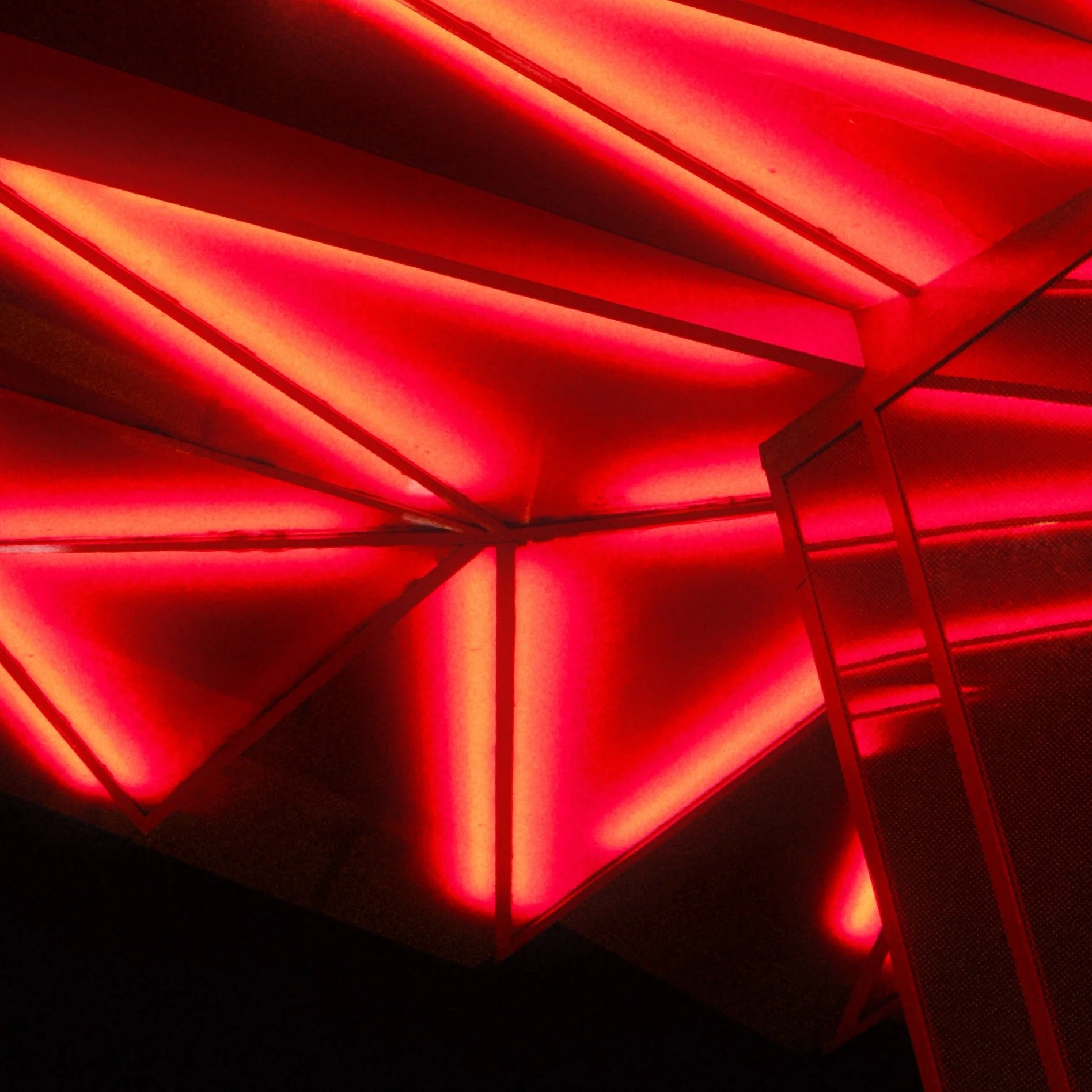 Structure géométrique en acier avec éclairage rouge, formant un motif moderne et abstrait.