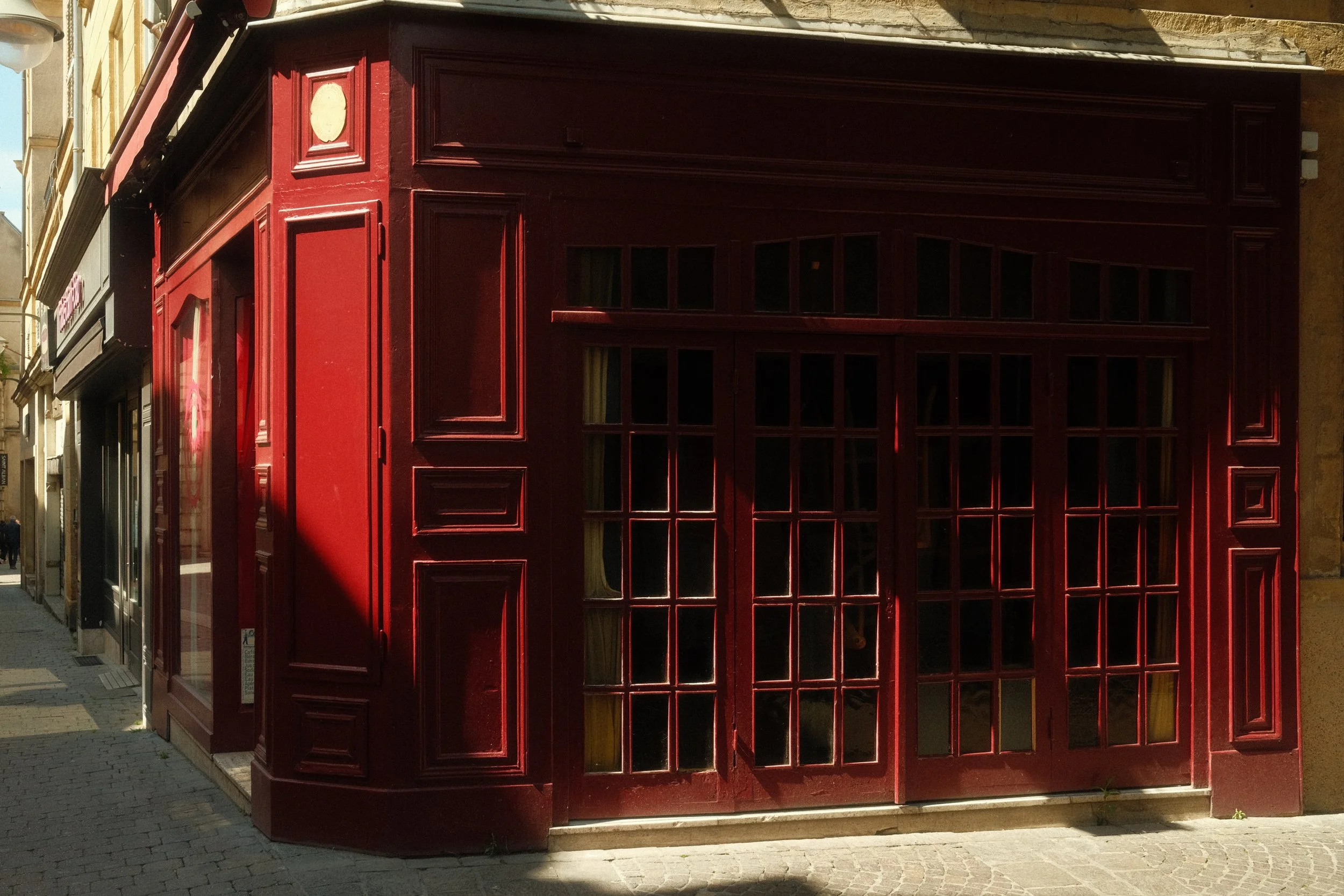 Vue d'une façade de boutique avec une grande porte en bois rouge avec plusieurs petites fenêtres en verre, située dans une rue pavée