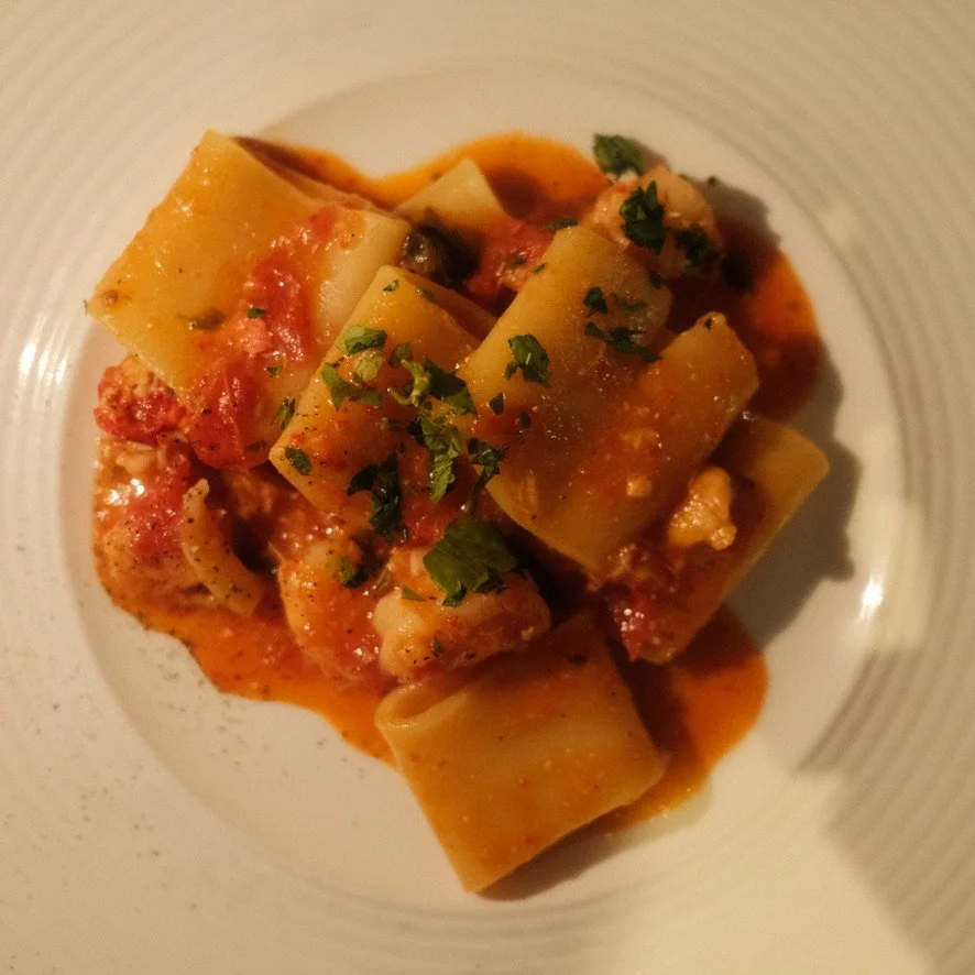 Raviolis de pasta large garnis de sauce tomate et de fines herbes dans une assiette blanche.