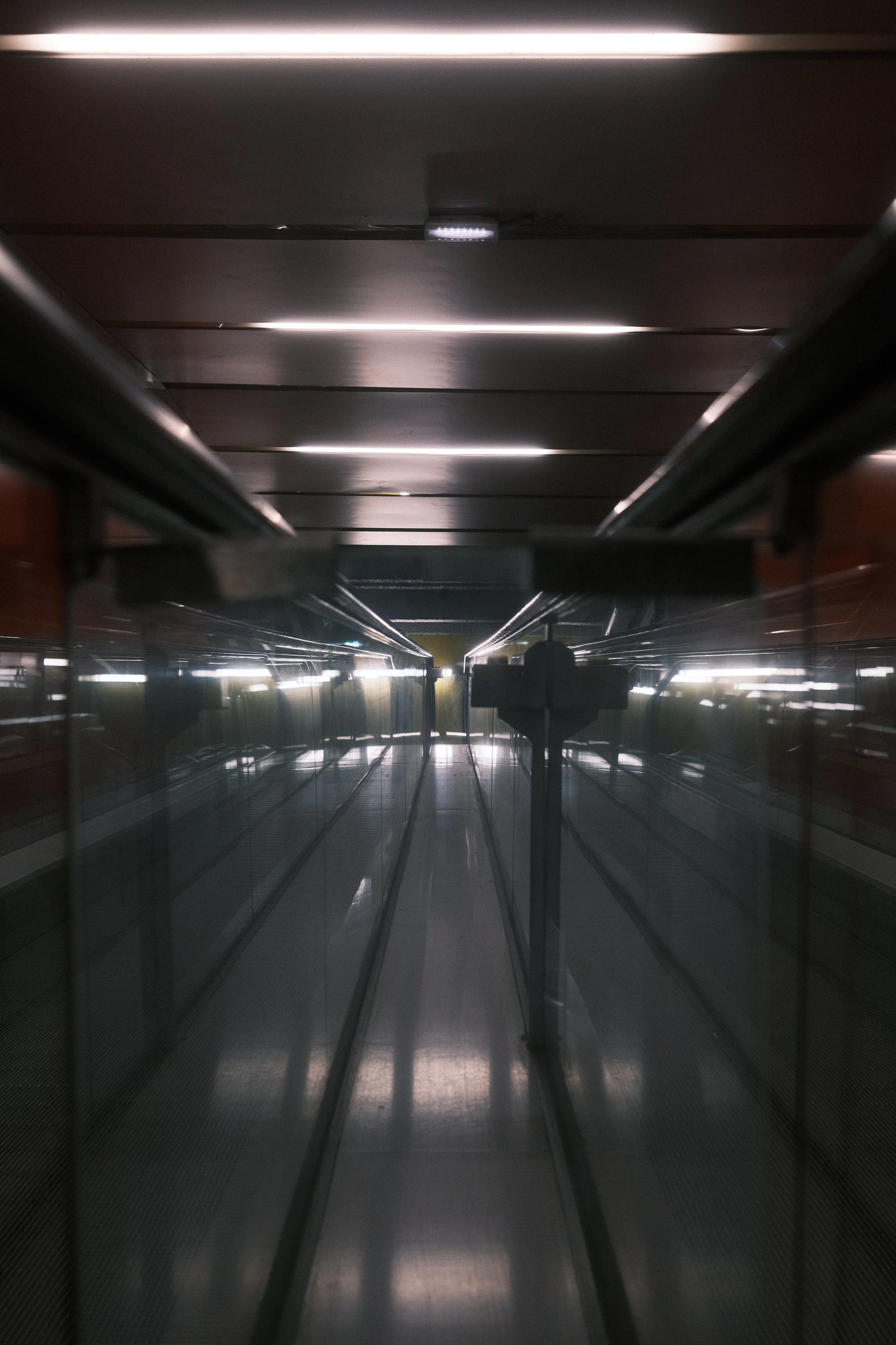 Un passage futuriste avec un sol en métal, des couloirs étroits et des murs en verre, avec un escalier au centre.