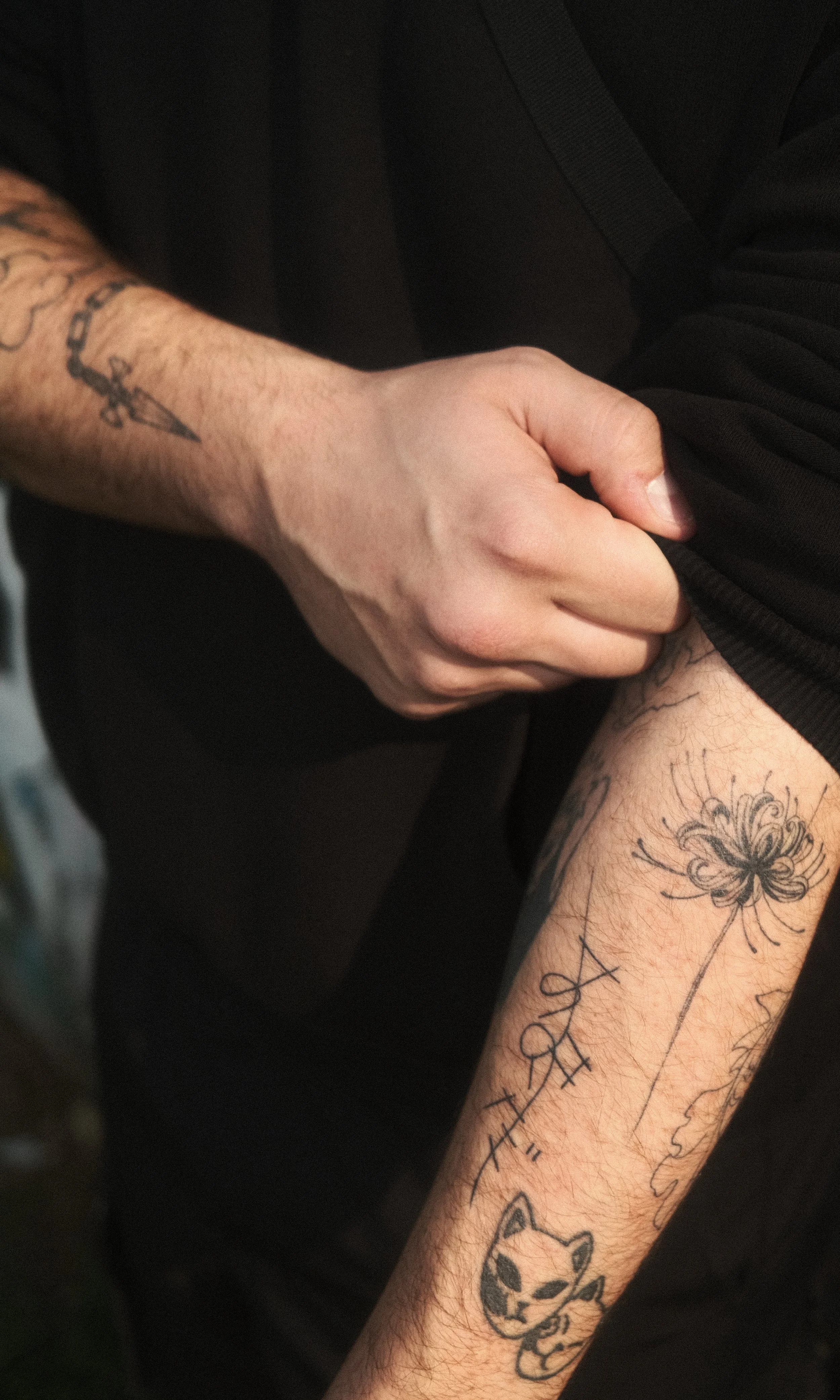 Une personne avec des tatouages sur le bras et la jambe, tenant le poignet de son propre bras avec la main gauche.