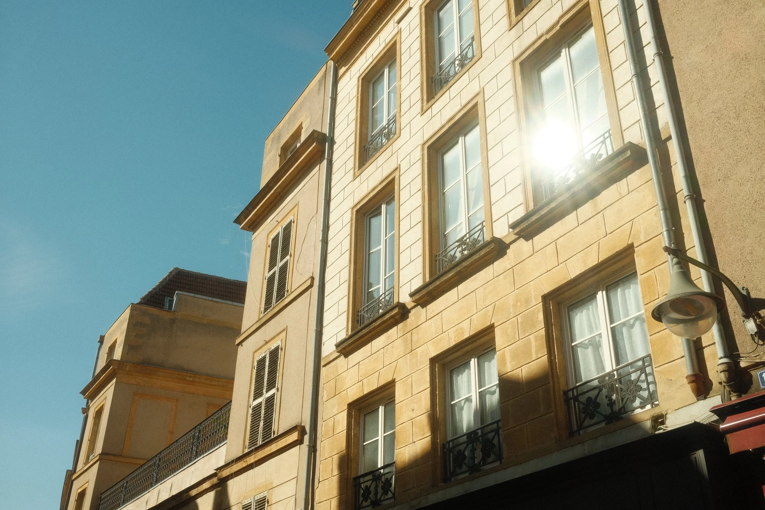 Bâtiments anciens avec des fenêtres à volets et des balcons en fer noir, ensoleillement brillant et ciel clair.