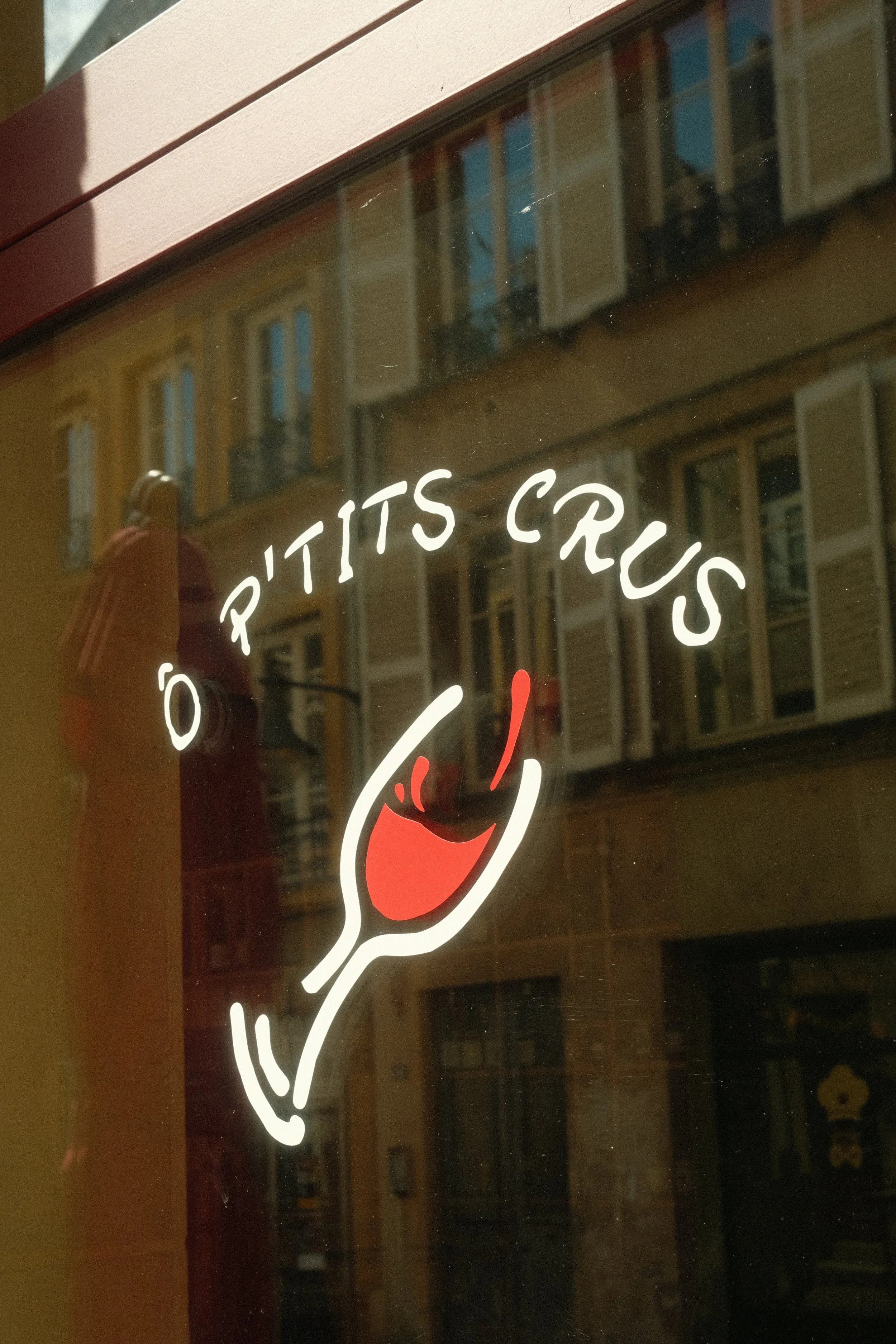 Logo de l'établissement 'O Pítits Crus' avec une main tenant un verre de vin rouge.