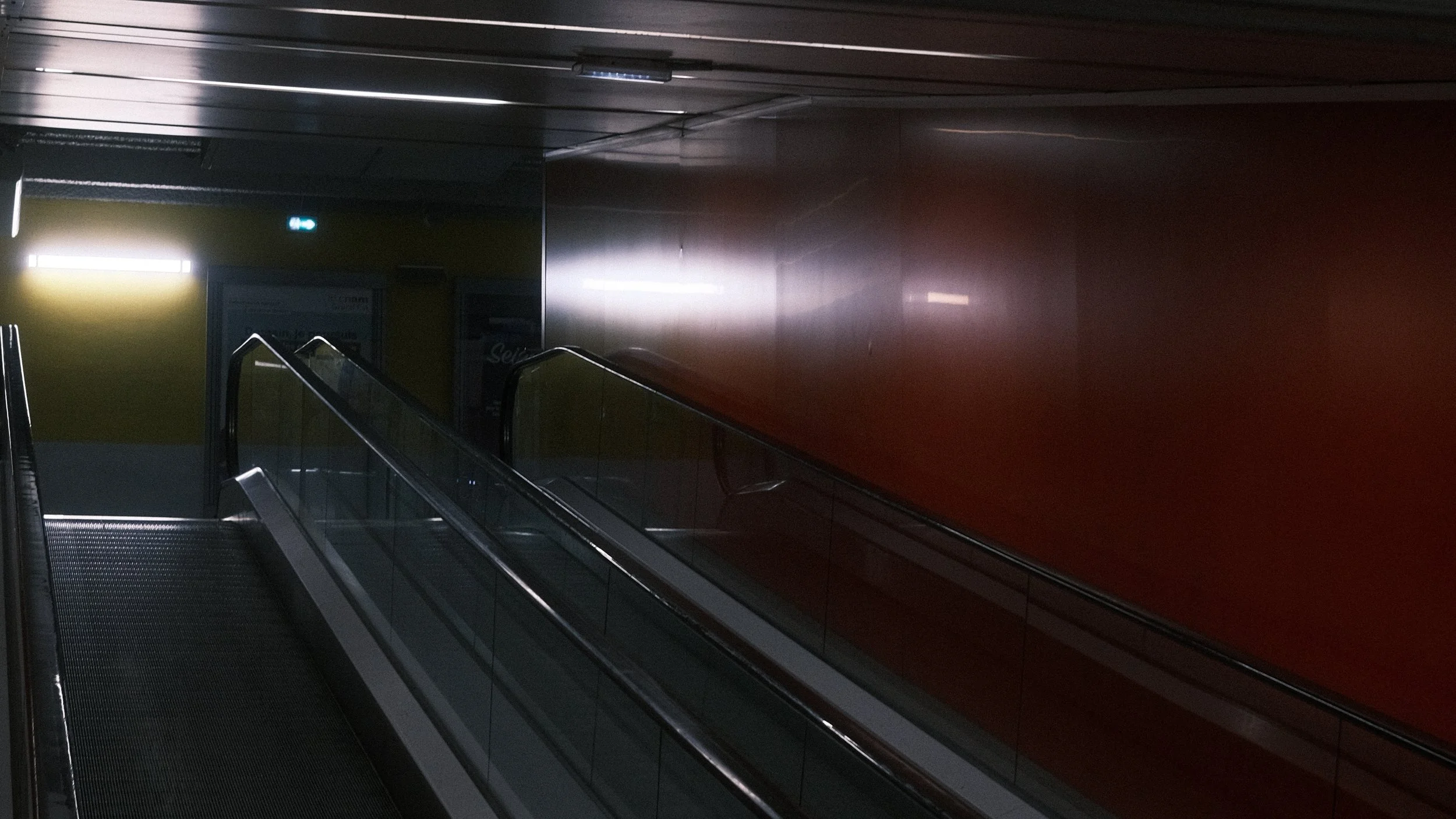 Escalator dans un passager souterrain, avec murs en verre, et éclairage discret.