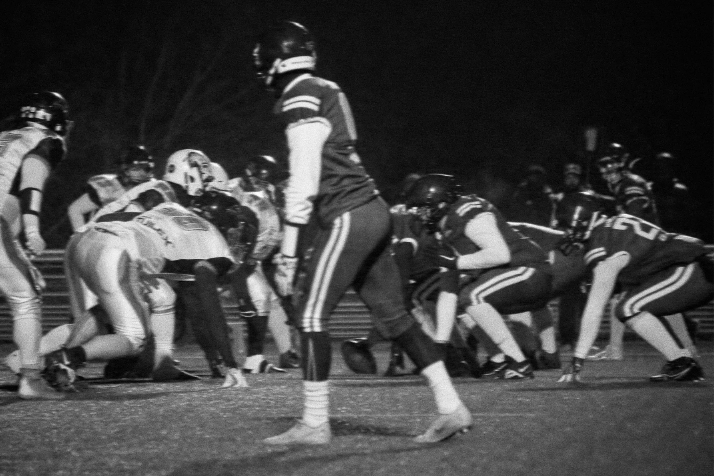 Une équipe de football américain en pleine action lors d'un match nocturne, en noir et blanc.
