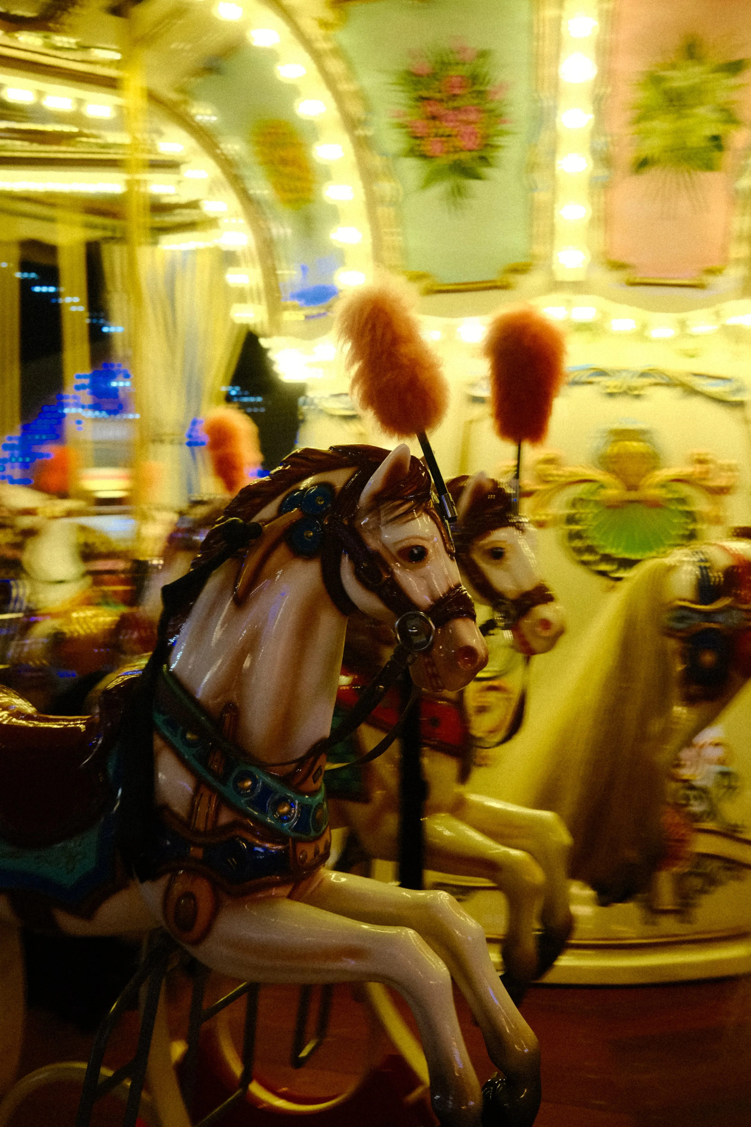 Cheval en jouet sur un manège de fête foraine avec lumières colorées et décorations florales en arrière-plan.