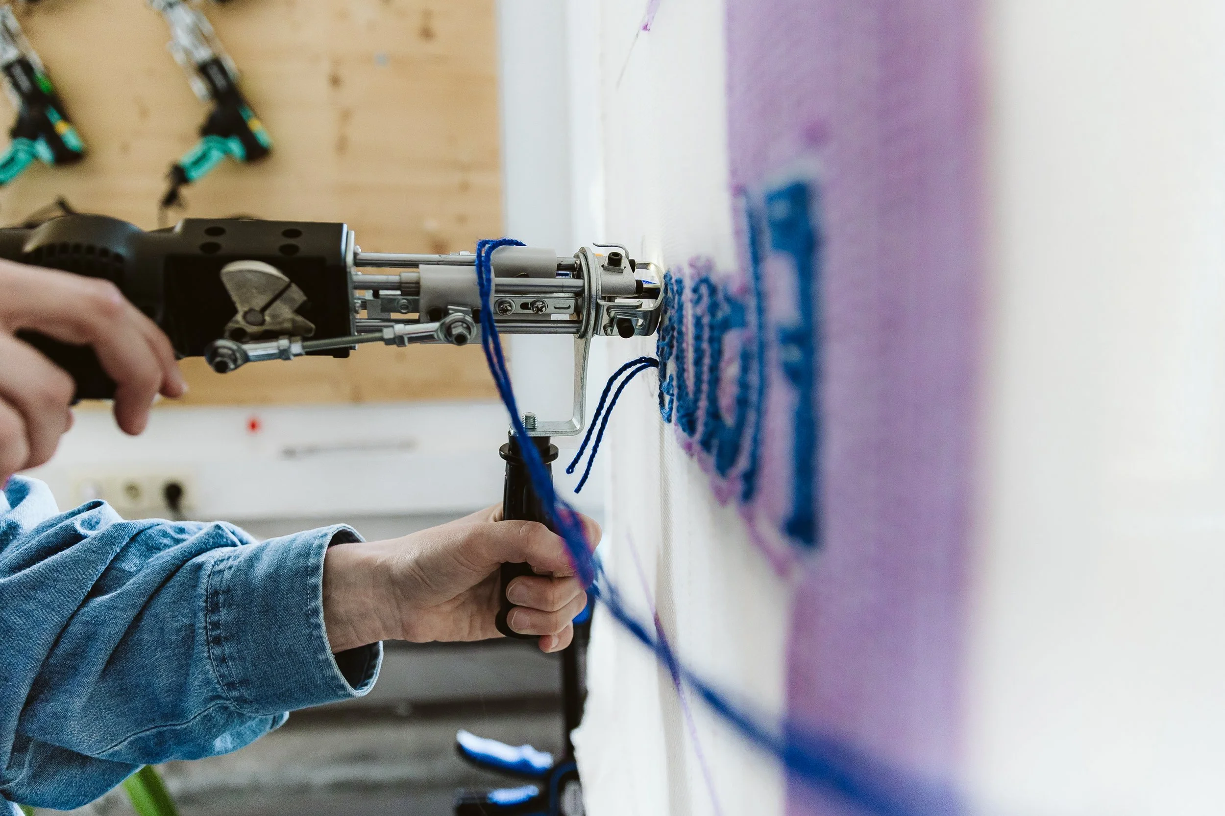 Eine Hand hält einen Bohrer, der auf eine Wand gerichtet ist, während blaue Schnüre an der Wand befestigt sind.
