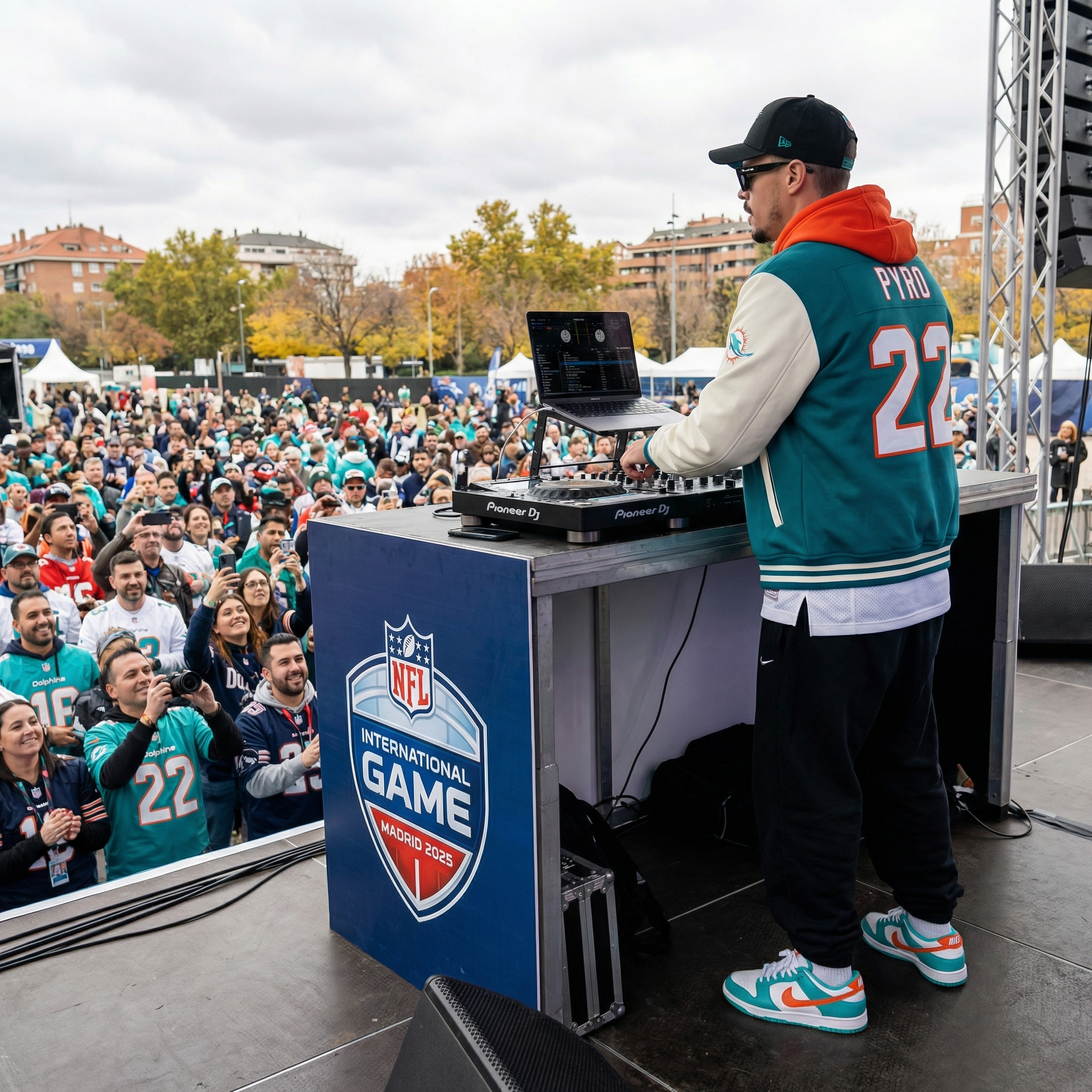 DJ Chris PyRo spielt auf einer Bühne beim NFL International Game in Madrid 2025, während eine große Menschenmenge im Freien zuschaut, verkleidet in Miami Dolphins und New England Patriots Jerseys, bei sonnigem aber bewölktem Wetter.