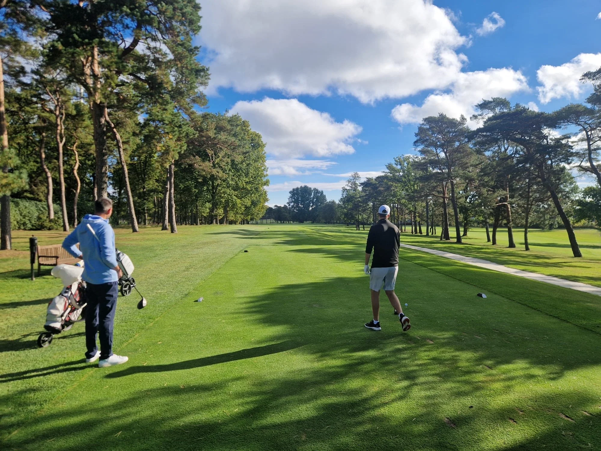 Sebastian Heijdenberg begleitet einen Golfer auf dem Abschlag eines bewaldeten Golfplatzes.