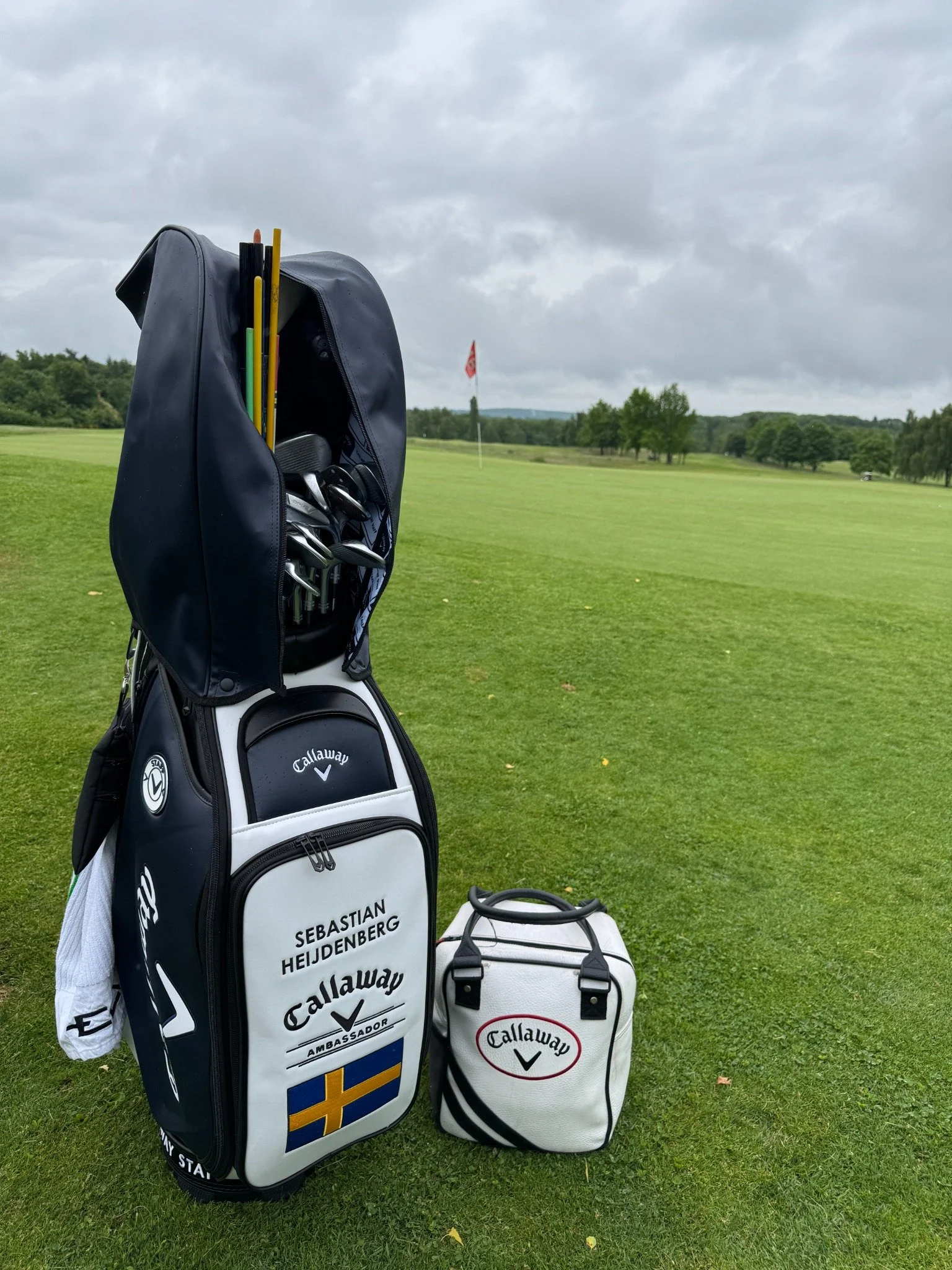 Golfbag mit Schlägern auf dem Golfplatz und einer Fahne im Hintergrund.