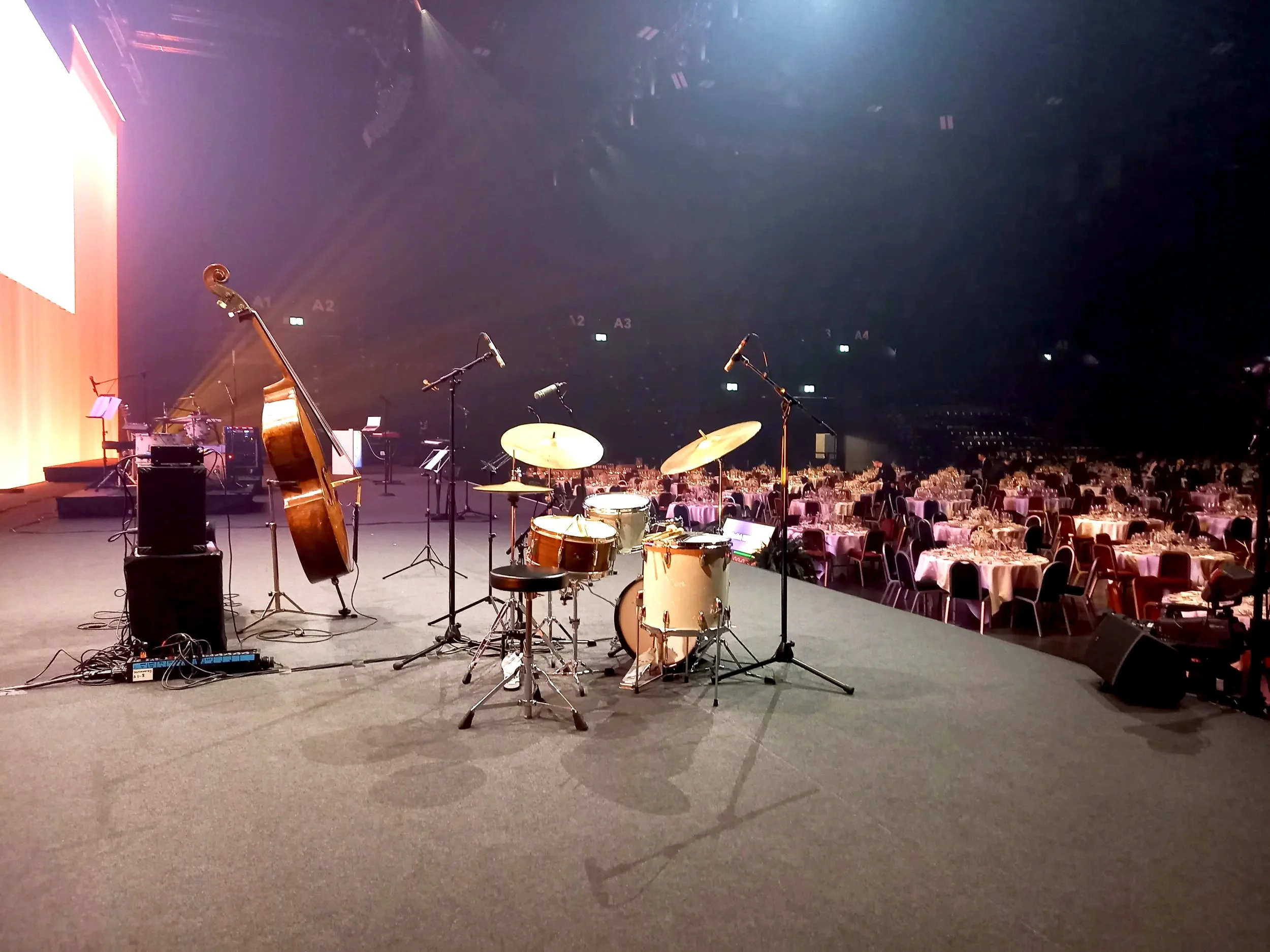 Auf der Bühne in der St. Jakobshalle in Basel sind Musikinstrumente von der Jazzband The Slick Notes, vor dem Saal mit zahlreichen gedeckten Tischen.